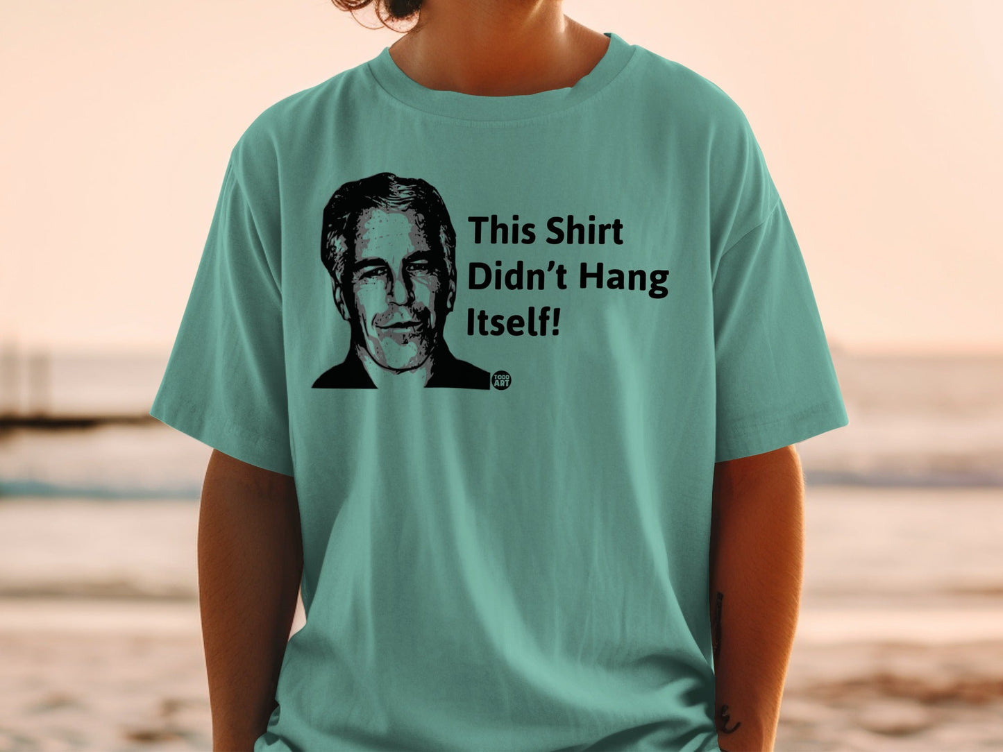 Teal t-shirt with black graphic of man's portrait and text "This Shirt Didn't Hang Itself!".