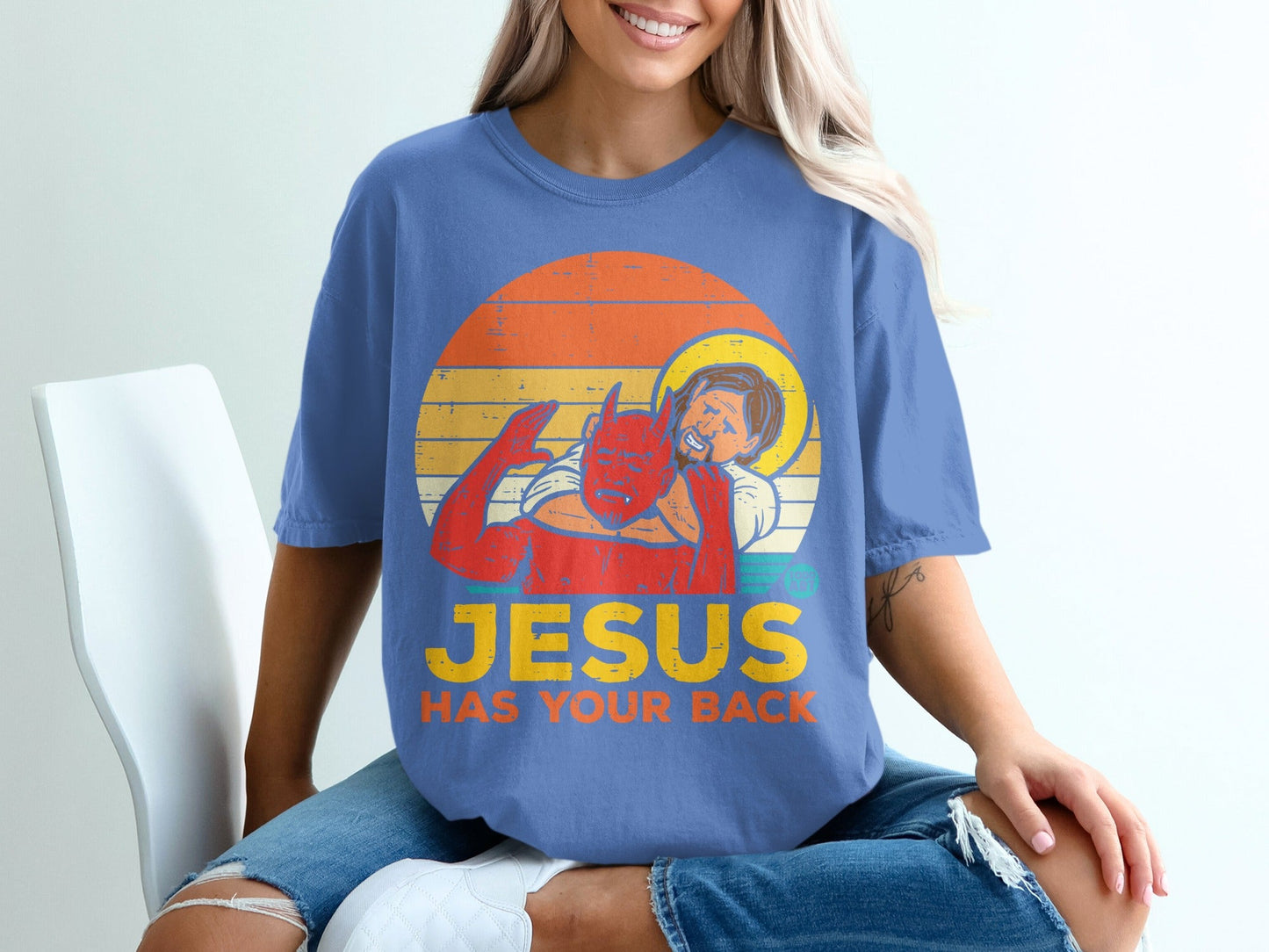 Devil with halo embraces person wearing "Jesus Has Your Back" t-shirt.