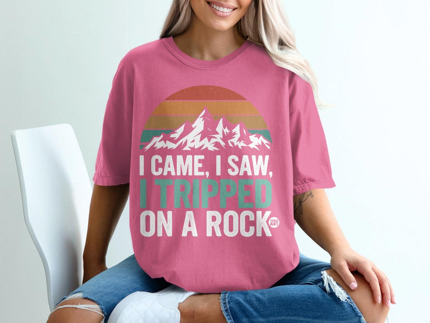 Pink t-shirt with "I came, I saw, I tripped on a rock" and mountain graphic.