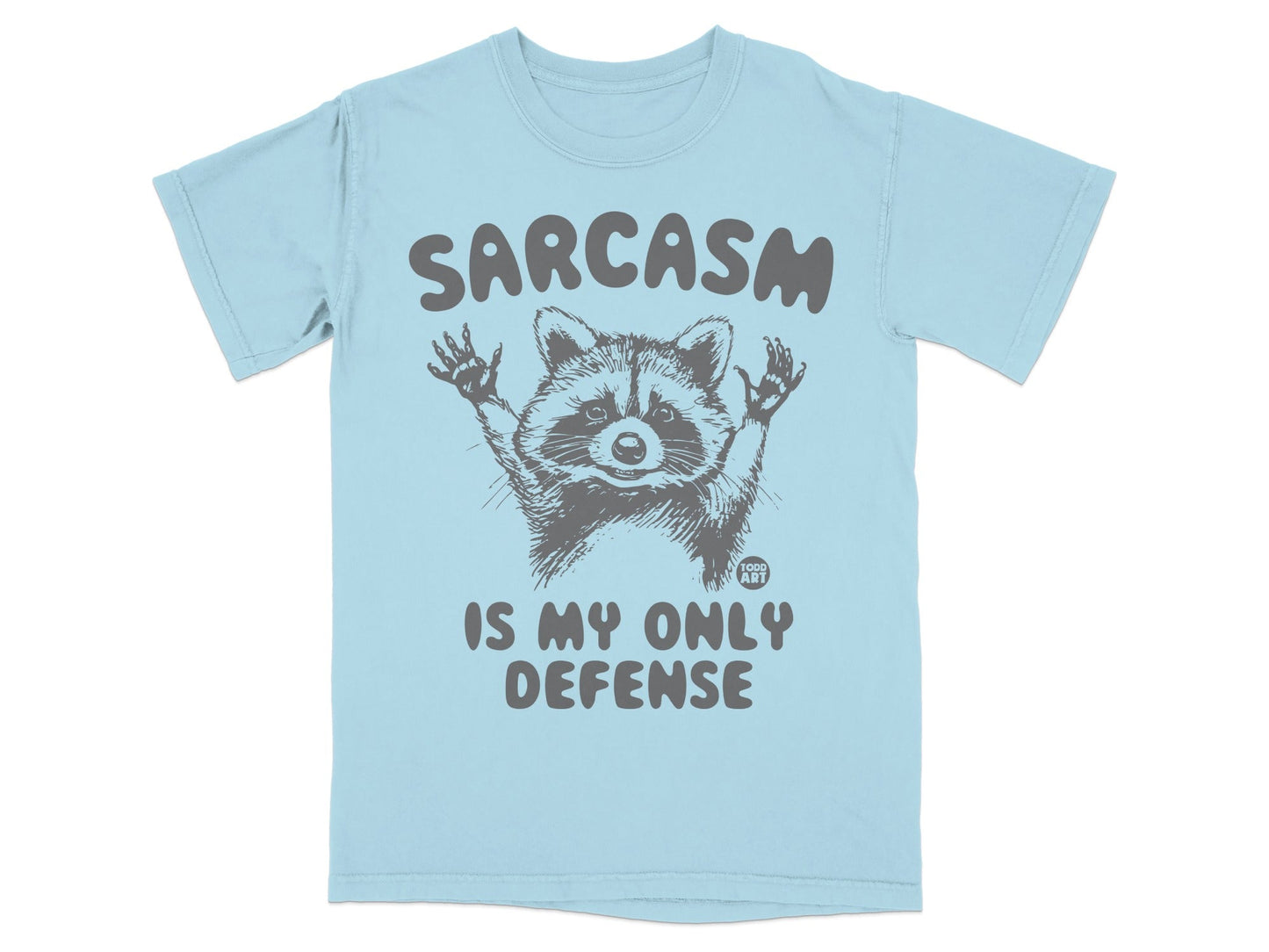 Light blue t-shirt with graphic of a raccoon and text "SARCASM IS MY ONLY DEFENSE".