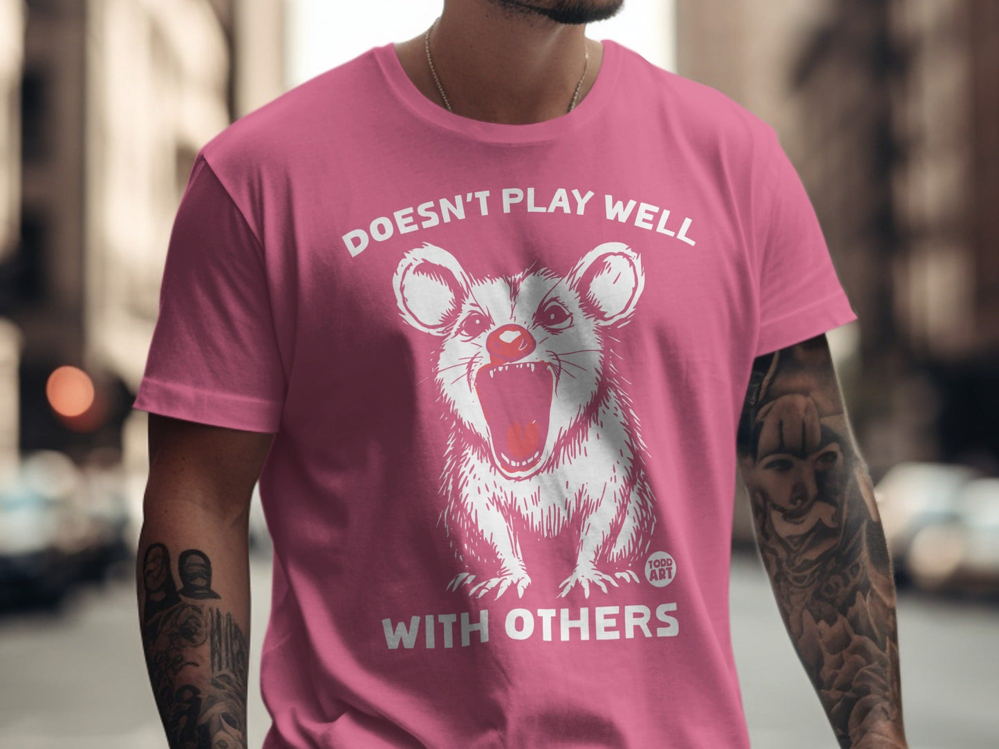Pink t-shirt with white graphic of a rat-like creature and text "Doesn't Play Well With Others".