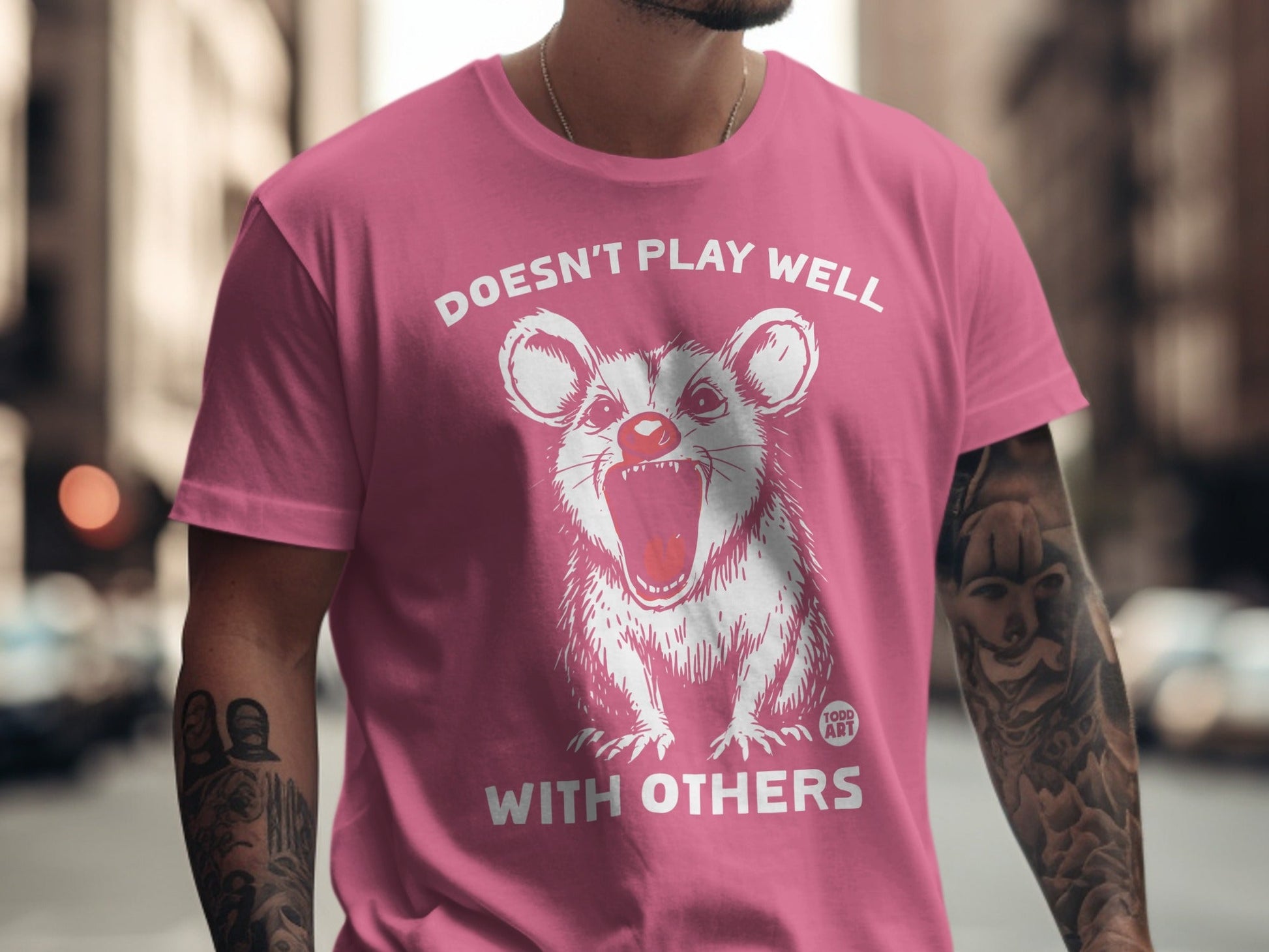 Pink t-shirt with white graphic of a rat-like creature and text "Doesn't Play Well With Others".