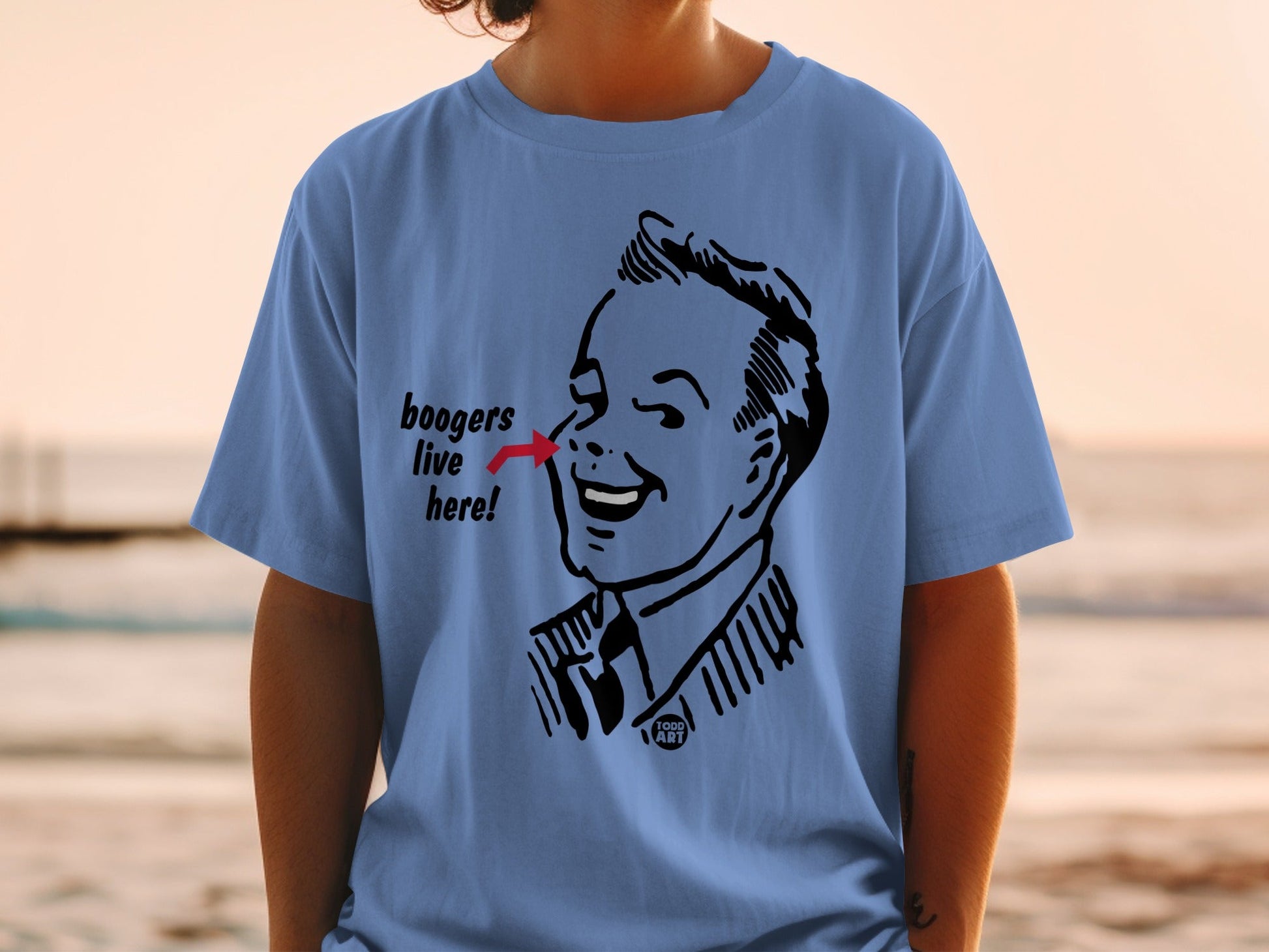 T-shirt with cartoon drawing of man pointing to nose, saying "boogers live here".