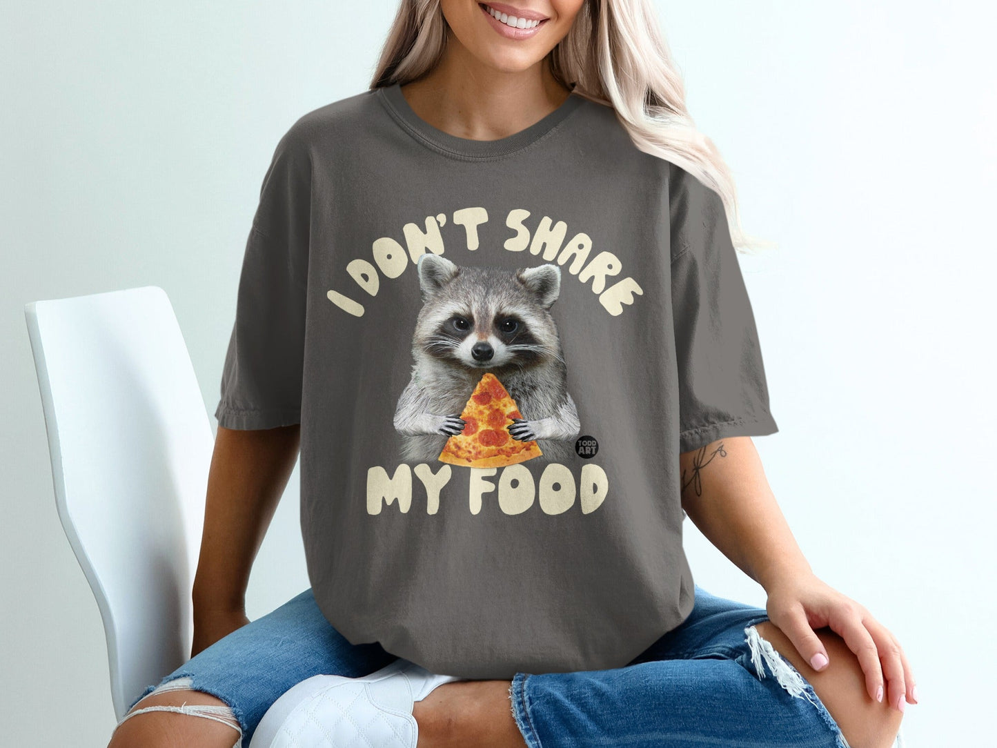 Woman in dark grey t-shirt with raccoon holding pizza and text "I DON'T SHARE MY FOOD".