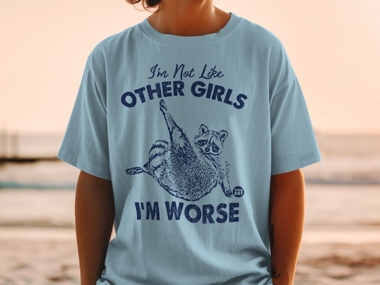 Light blue t-shirt with raccoon graphic and text "I'm Not Like Other Girls I'M WORSE".