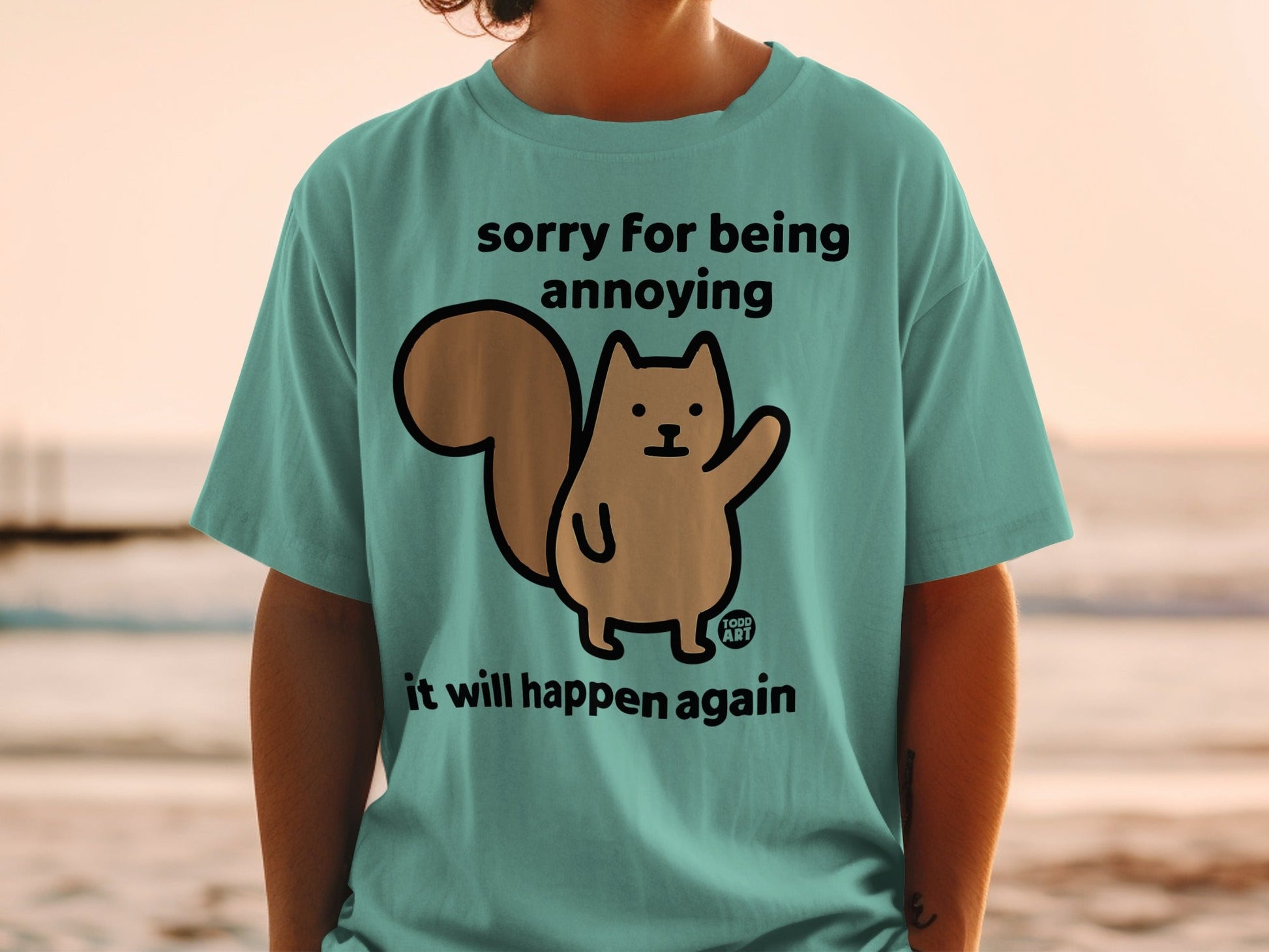 Teal t-shirt with a cartoon squirrel and text "sorry for being annoying it will happen again."