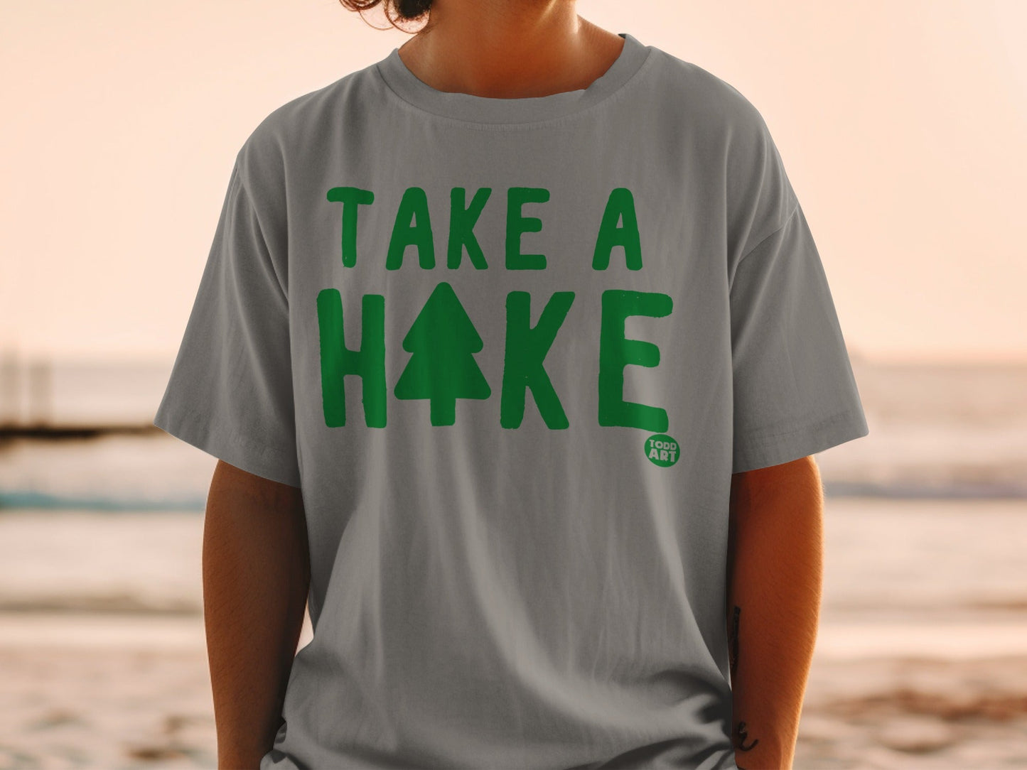 Grey t-shirt with green text "TAKE A HAKE" and a small pine tree icon.