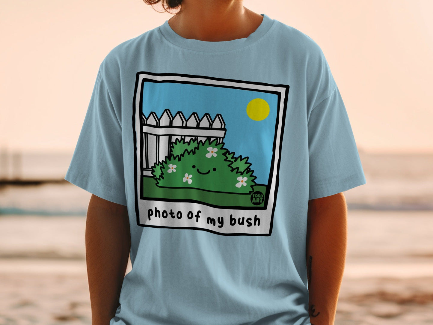 Light blue t-shirt with a cartoon bush and fence illustration reading "photo of my bush".
