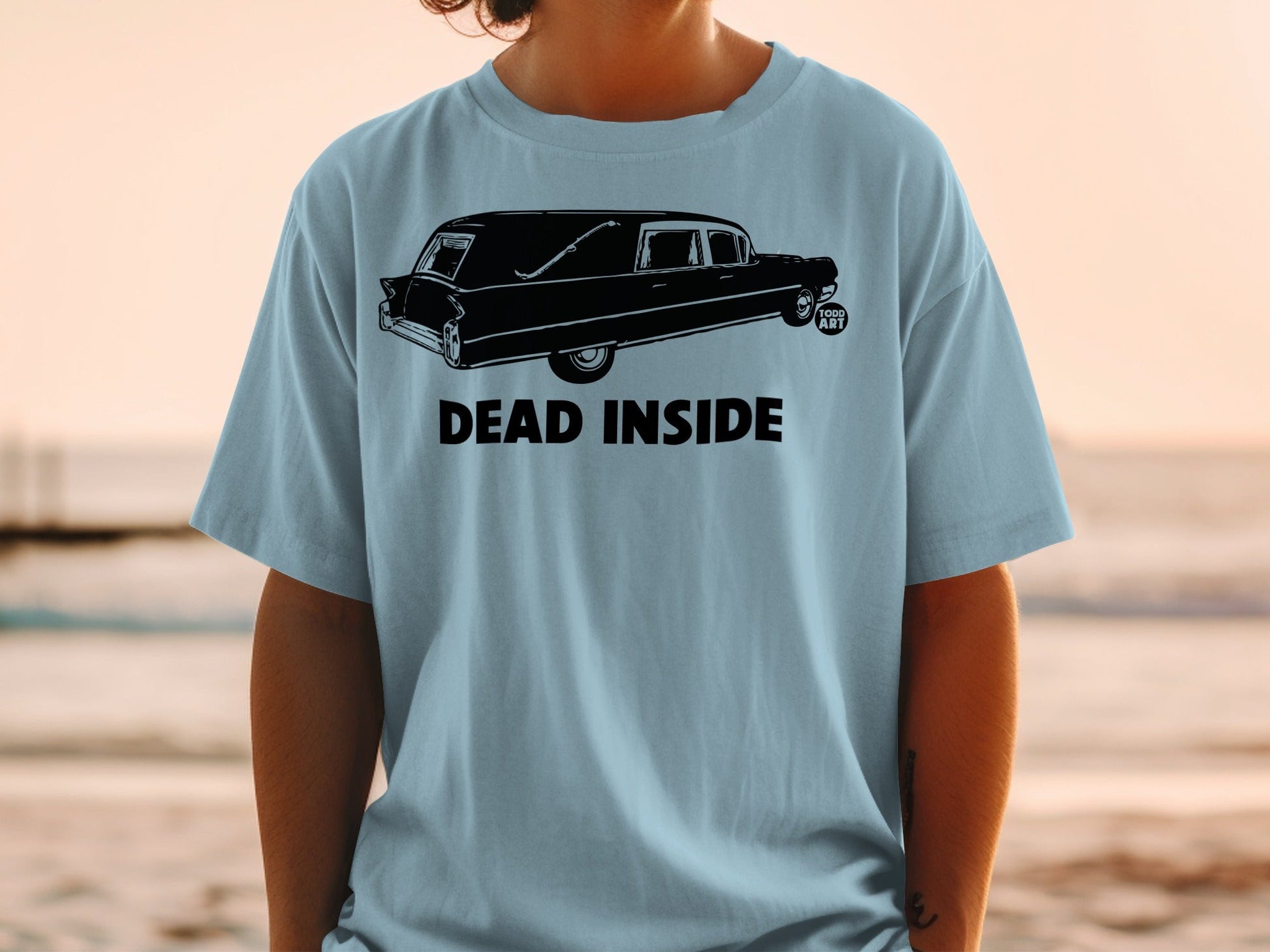 Light blue t-shirt with a black graphic of a hearse and the text "DEAD INSIDE".