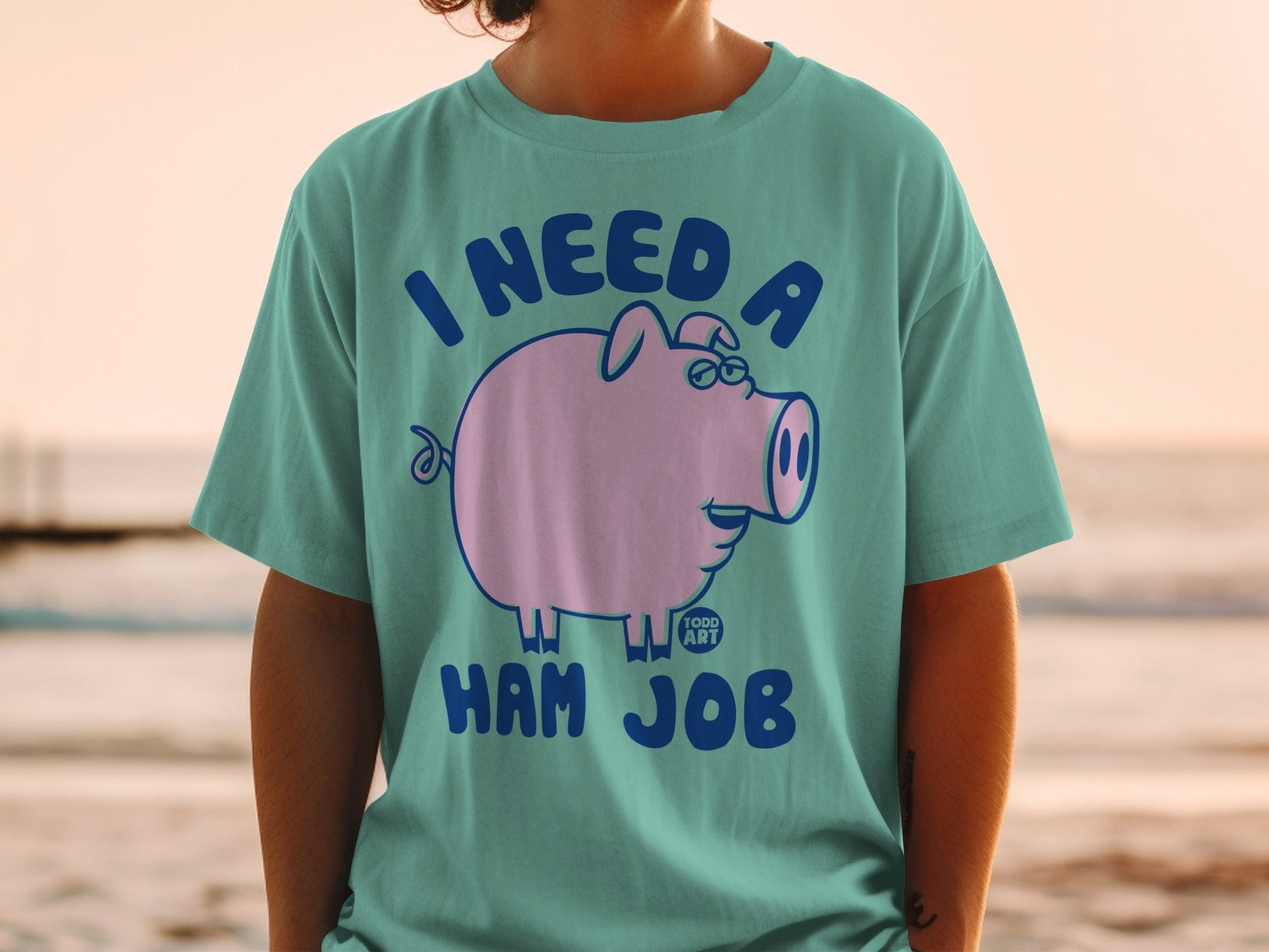 Teal t-shirt with a cartoon pig wearing glasses and text "I NEED A HAM JOB".