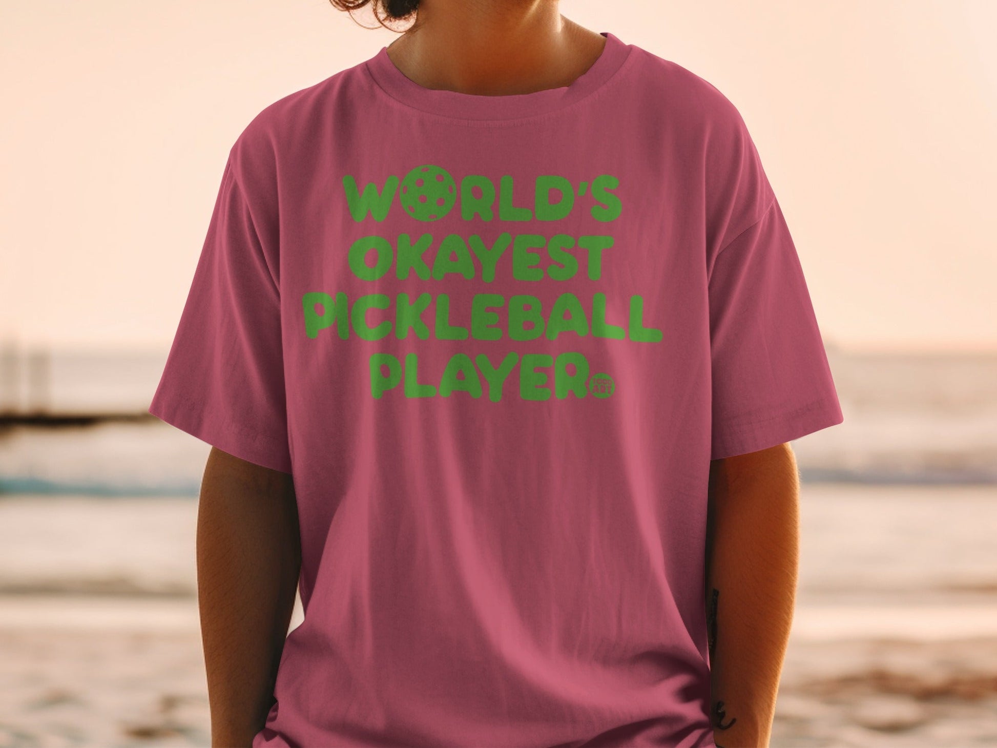 Pink t-shirt with "WORLD'S OKAYEST PICKLEBALL PLAYER" in green text.