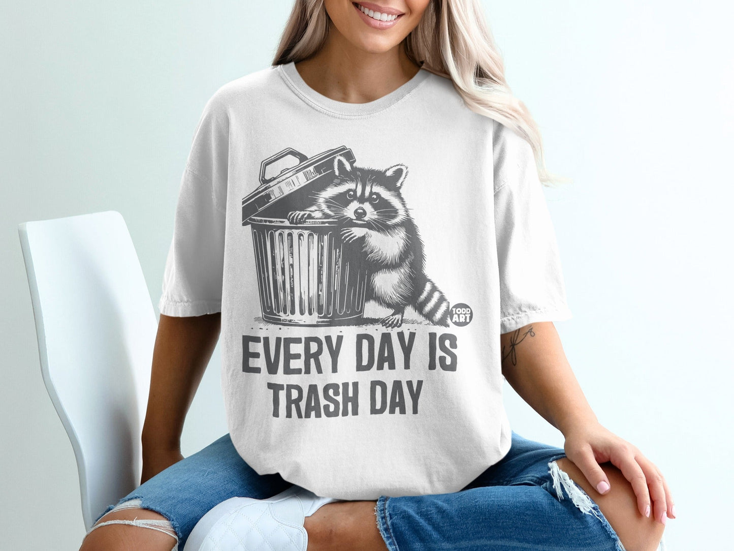 T-shirt with a raccoon peeking out of a trash can, text "Every day is trash day."