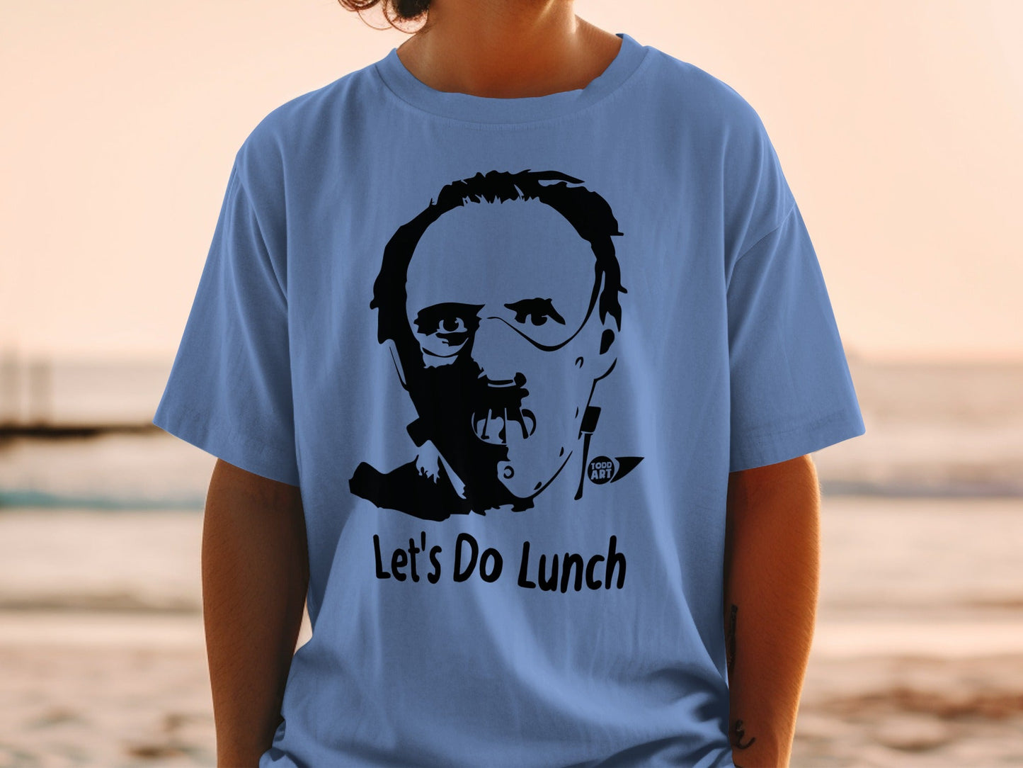 Blue t-shirt with a black graphic of Hannibal Lecter saying "Let's Do Lunch."