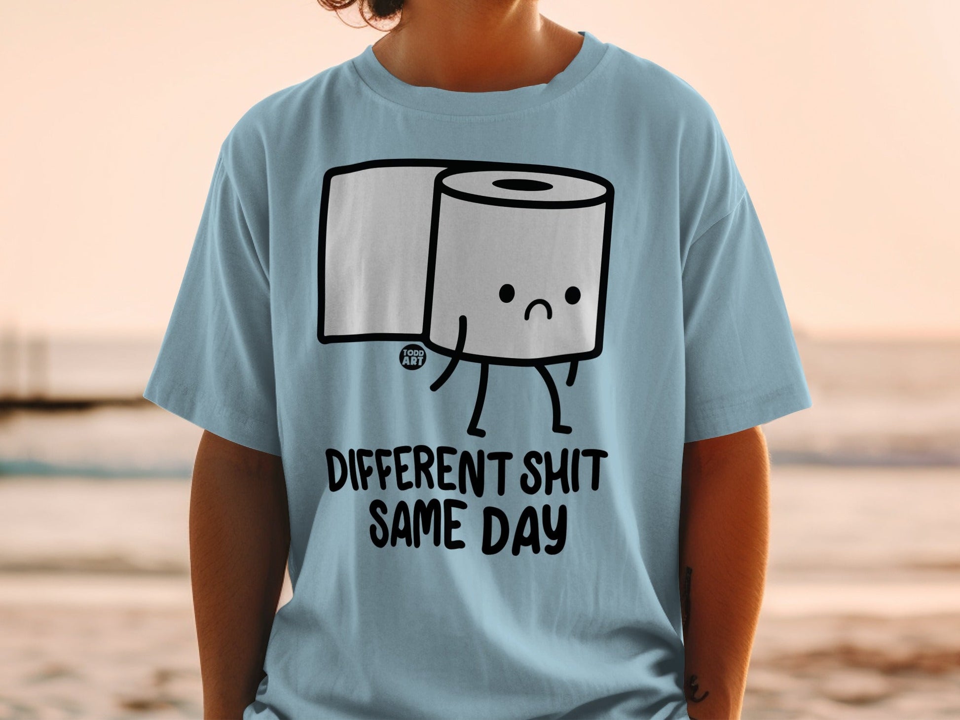 Light blue t-shirt with a cartoon toilet paper roll saying "DIFFERENT SHIT SAME DAY".
