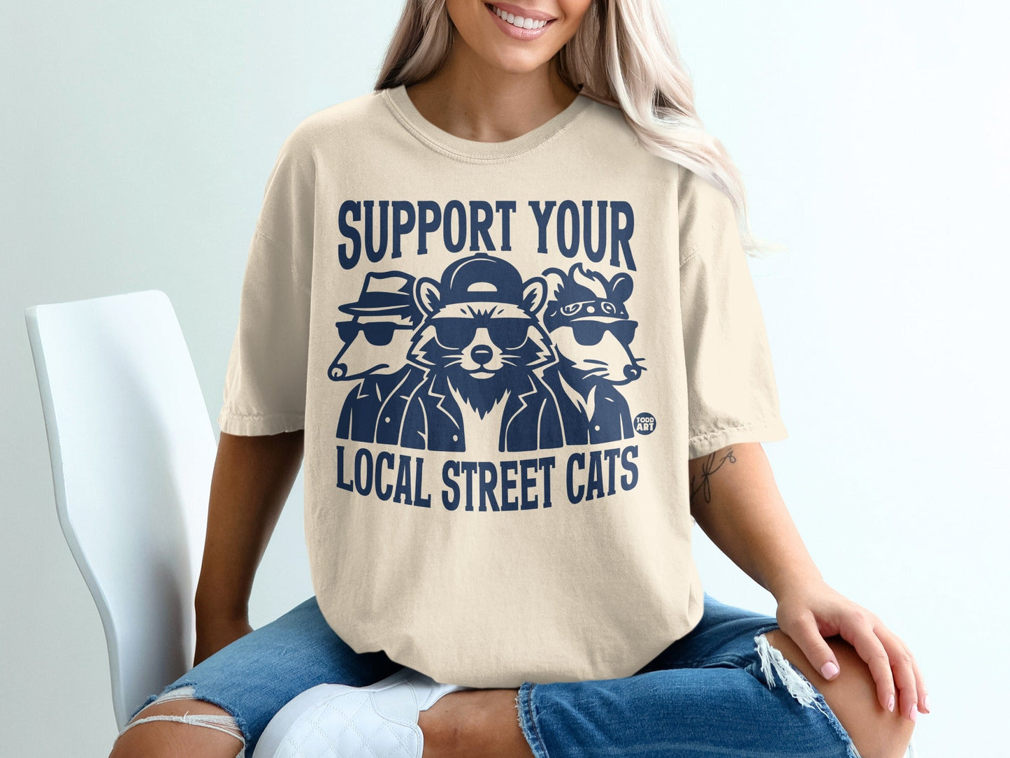 T-shirt with graphic of three raccoons in sunglasses and hats, text "SUPPORT YOUR LOCAL STREET CATS".