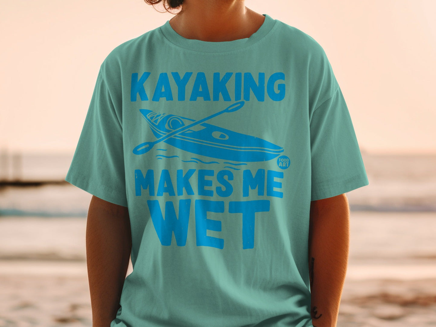 Teal t-shirt with a kayak and paddle graphic and text "Kayaking Makes Me Wet."