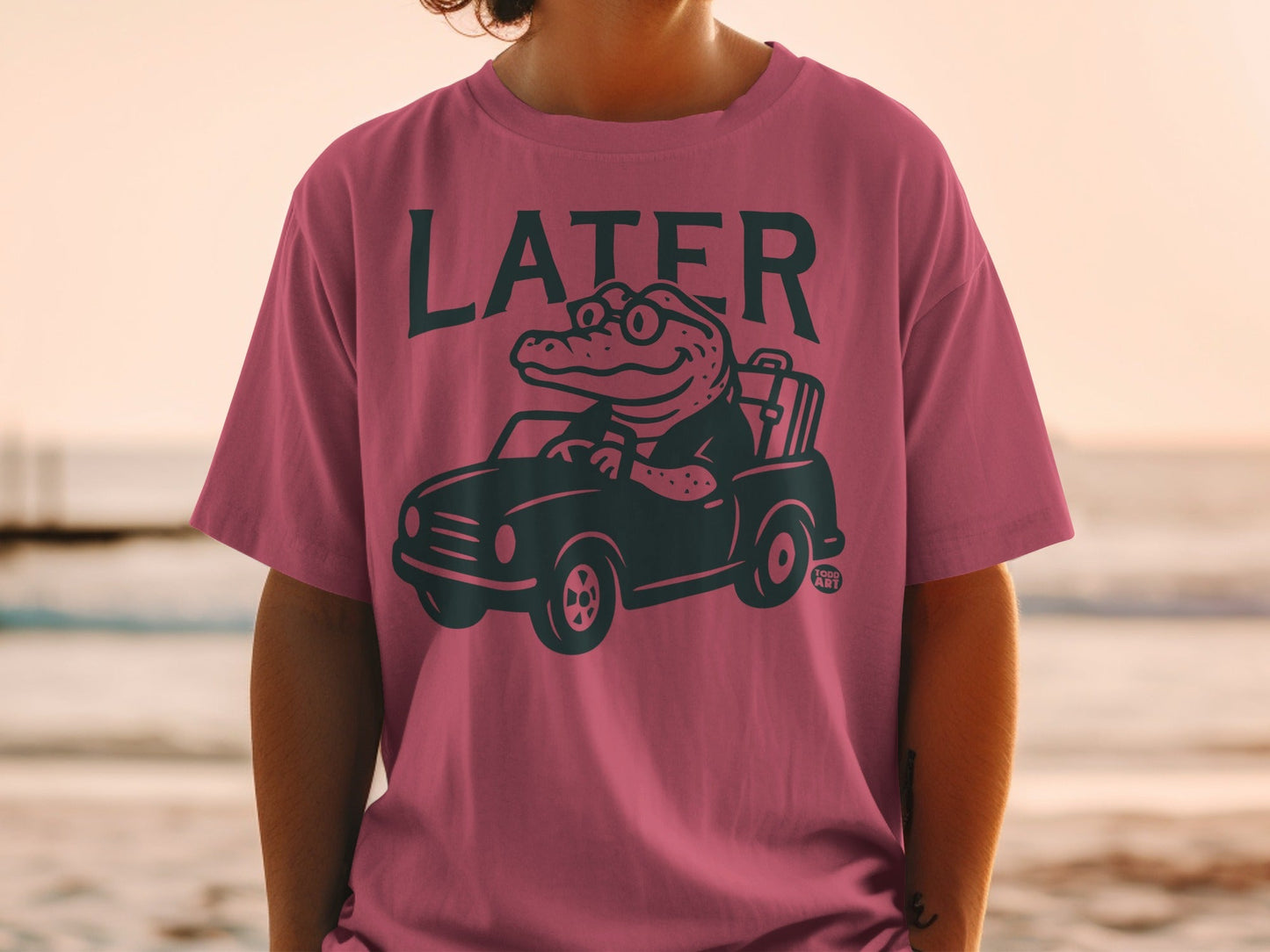 Man wearing pink t-shirt with a cartoon alligator driving a car.