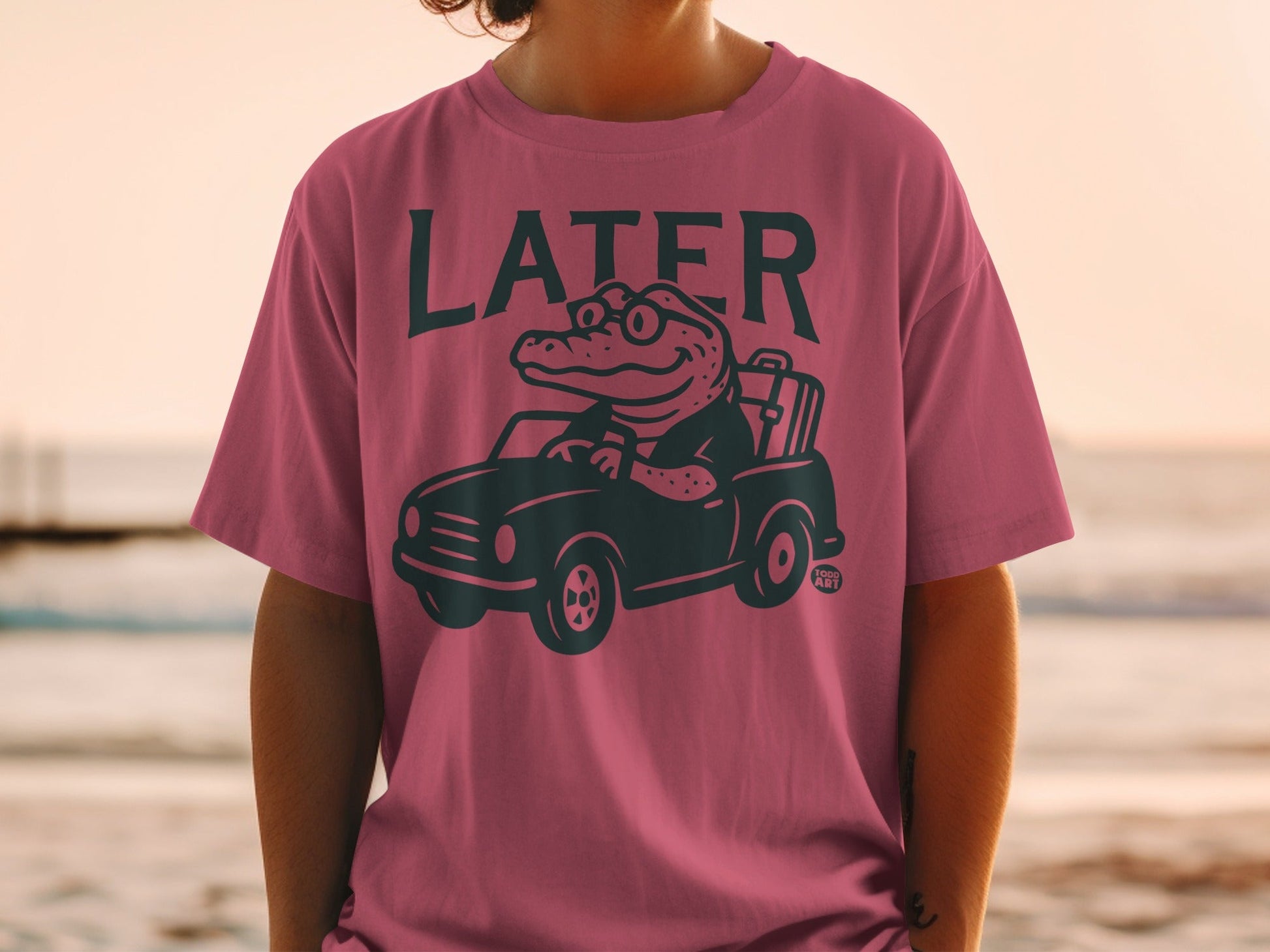 Man wearing pink t-shirt with a cartoon alligator driving a car.