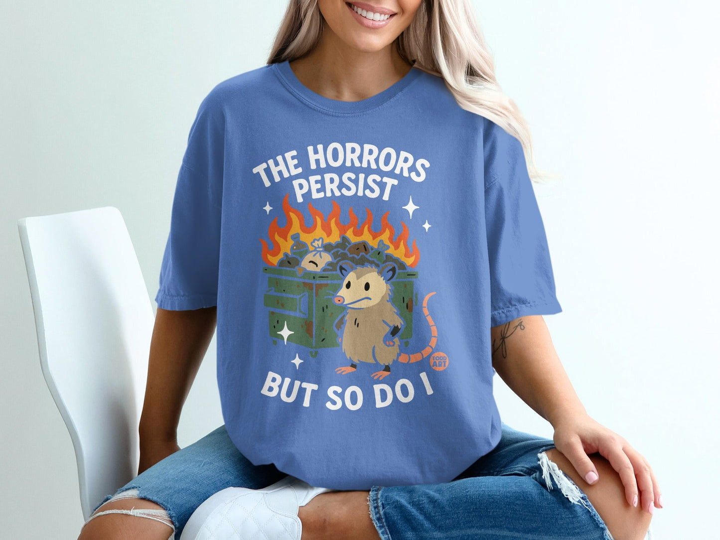 Blue t-shirt with "The Horrors Persist But So Do I" and a possum in a burning dumpster.
