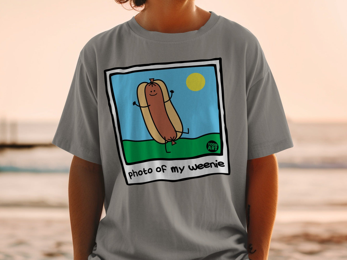 Cartoon hot dog with arms raised in a grassy field, text "photo of my weenie".