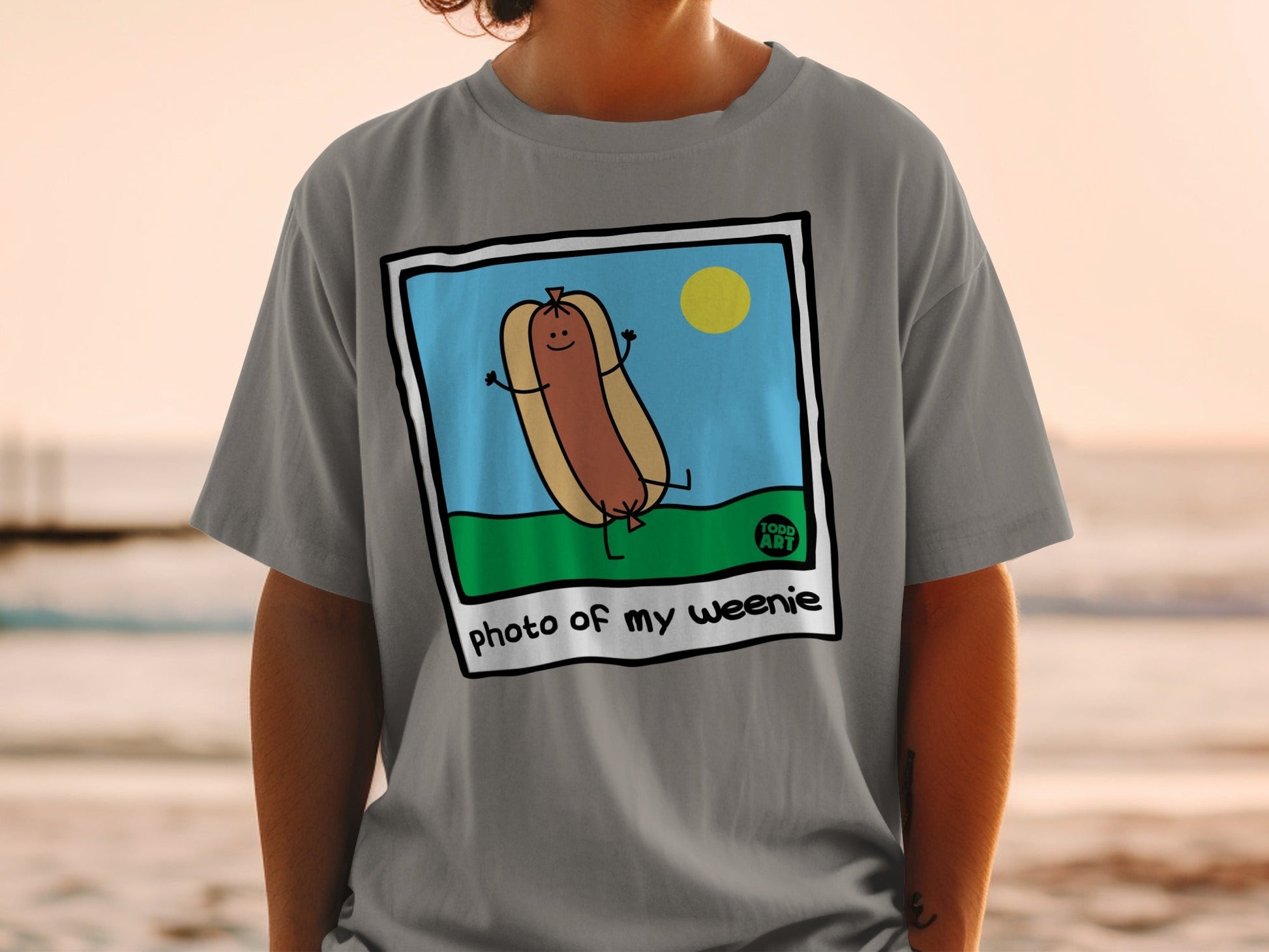 Cartoon hot dog with arms raised in a grassy field, text "photo of my weenie".
