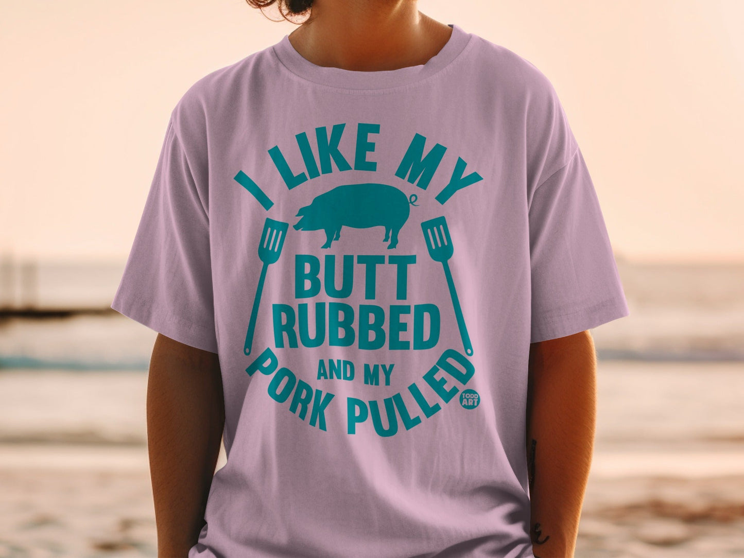 T-shirt with teal text and pig graphic: "I LIKE MY BUTT RUBBED AND MY PORK PULLED."