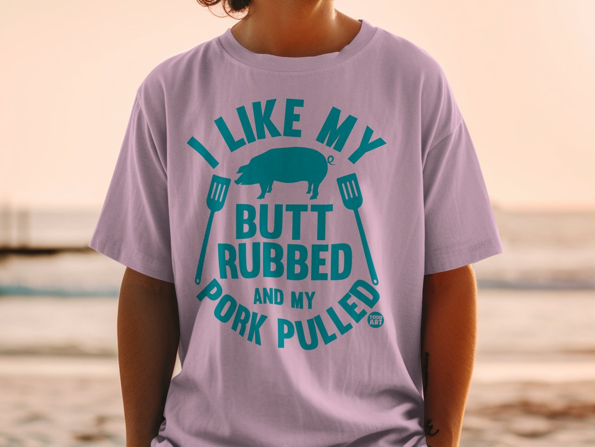 T-shirt with teal text and pig graphic: "I LIKE MY BUTT RUBBED AND MY PORK PULLED."