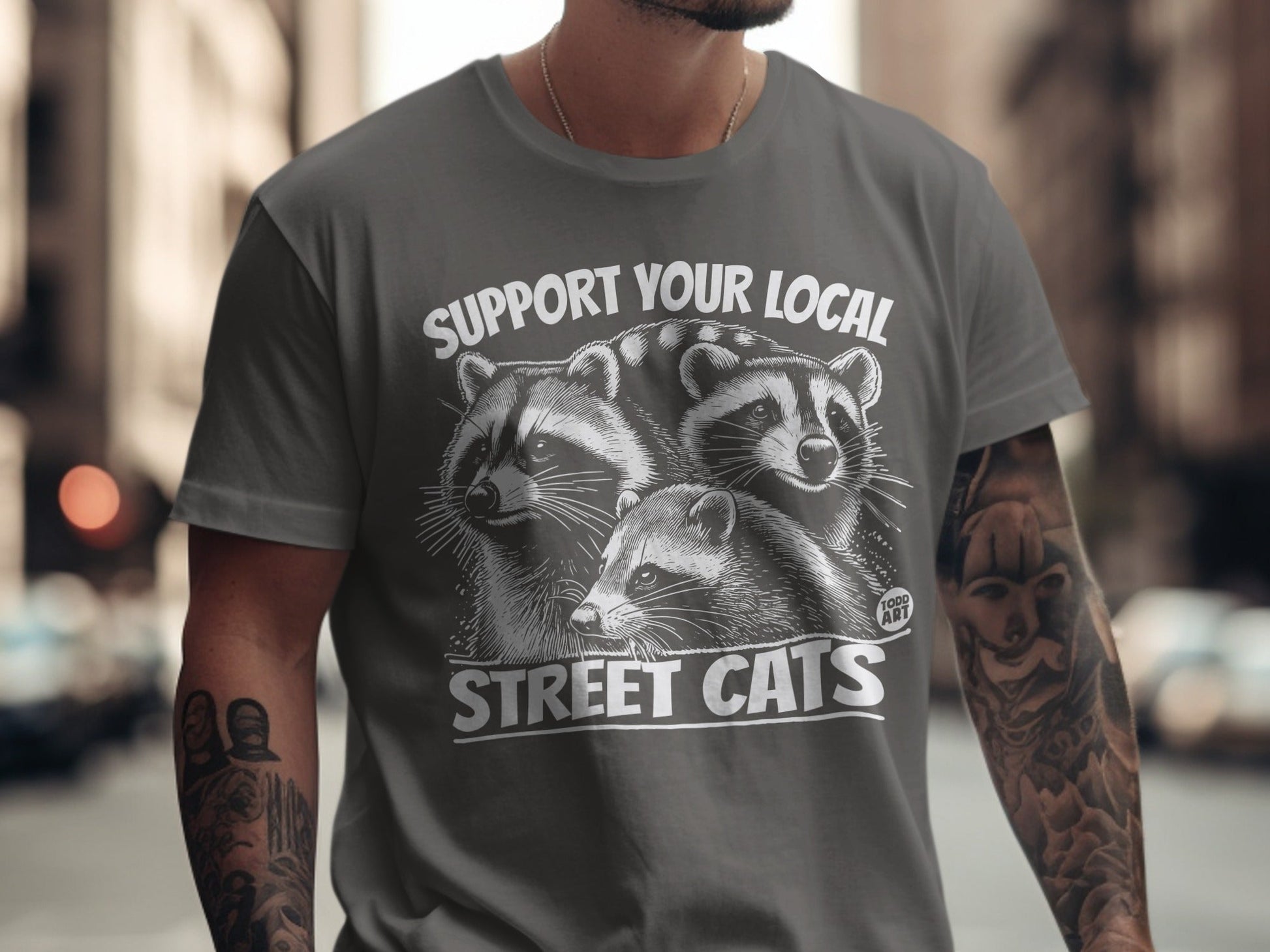 Grey t-shirt with three raccoons and text "SUPPORT YOUR LOCAL STREET CATS".