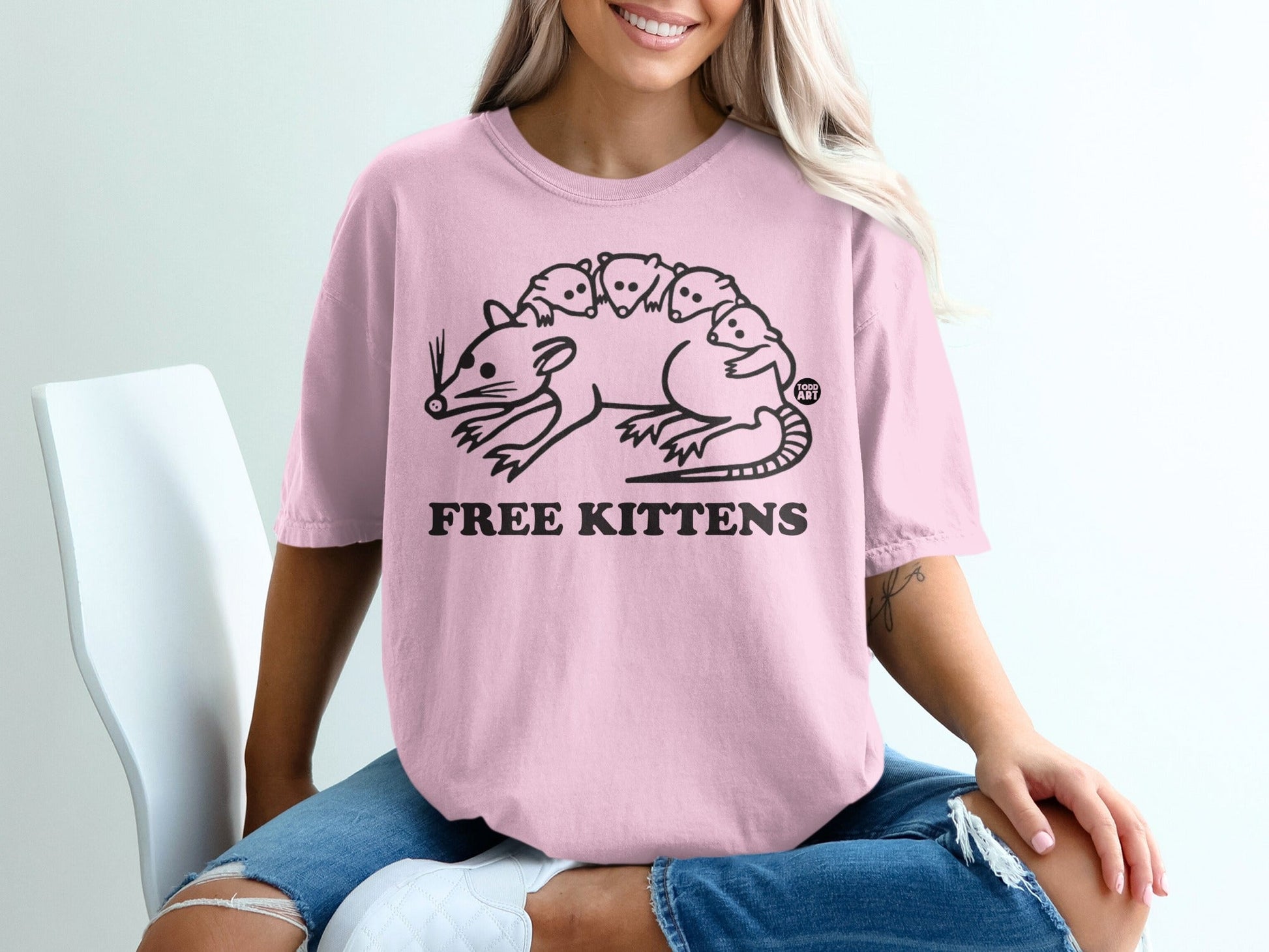Pink t-shirt with a stylized drawing of a rat carrying kittens and text "FREE KITTENS".