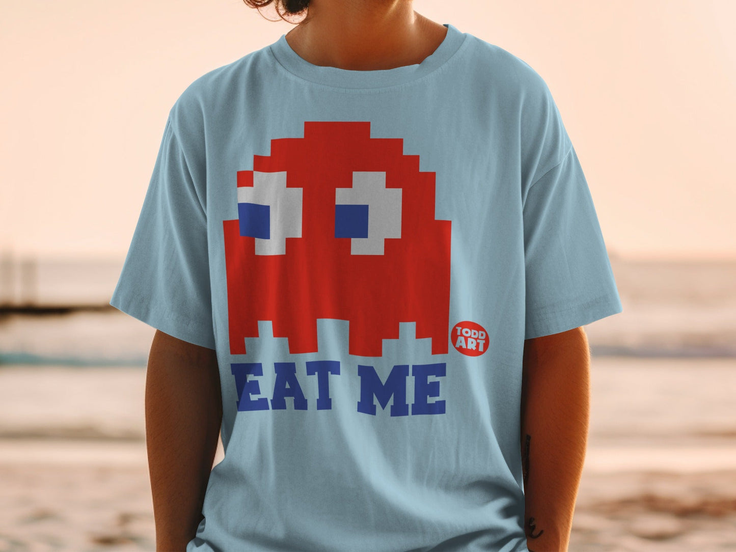 Light blue t-shirt with a red Pac-Man ghost and "EAT ME" text.