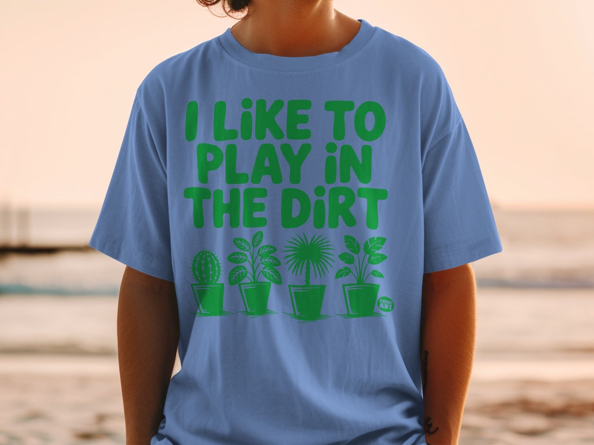 Blue t-shirt with green text "I LIKE TO PLAY IN THE DIRT" and potted plants.