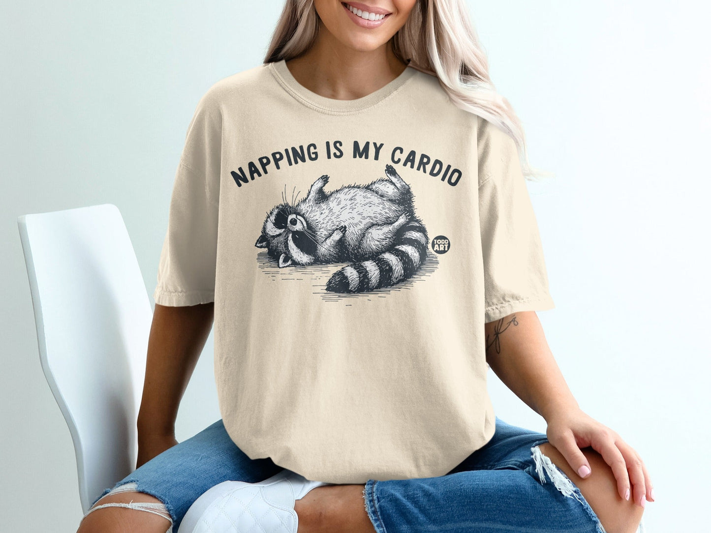 Cream t-shirt with a raccoon napping and "Napping is my cardio" text.