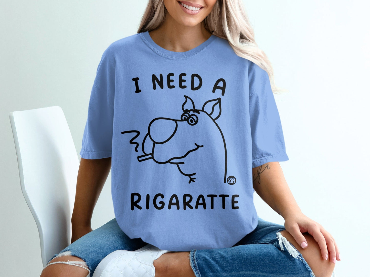 Light blue t-shirt with cartoon dog smoking cigarette and text "I NEED A RIGARETTE".