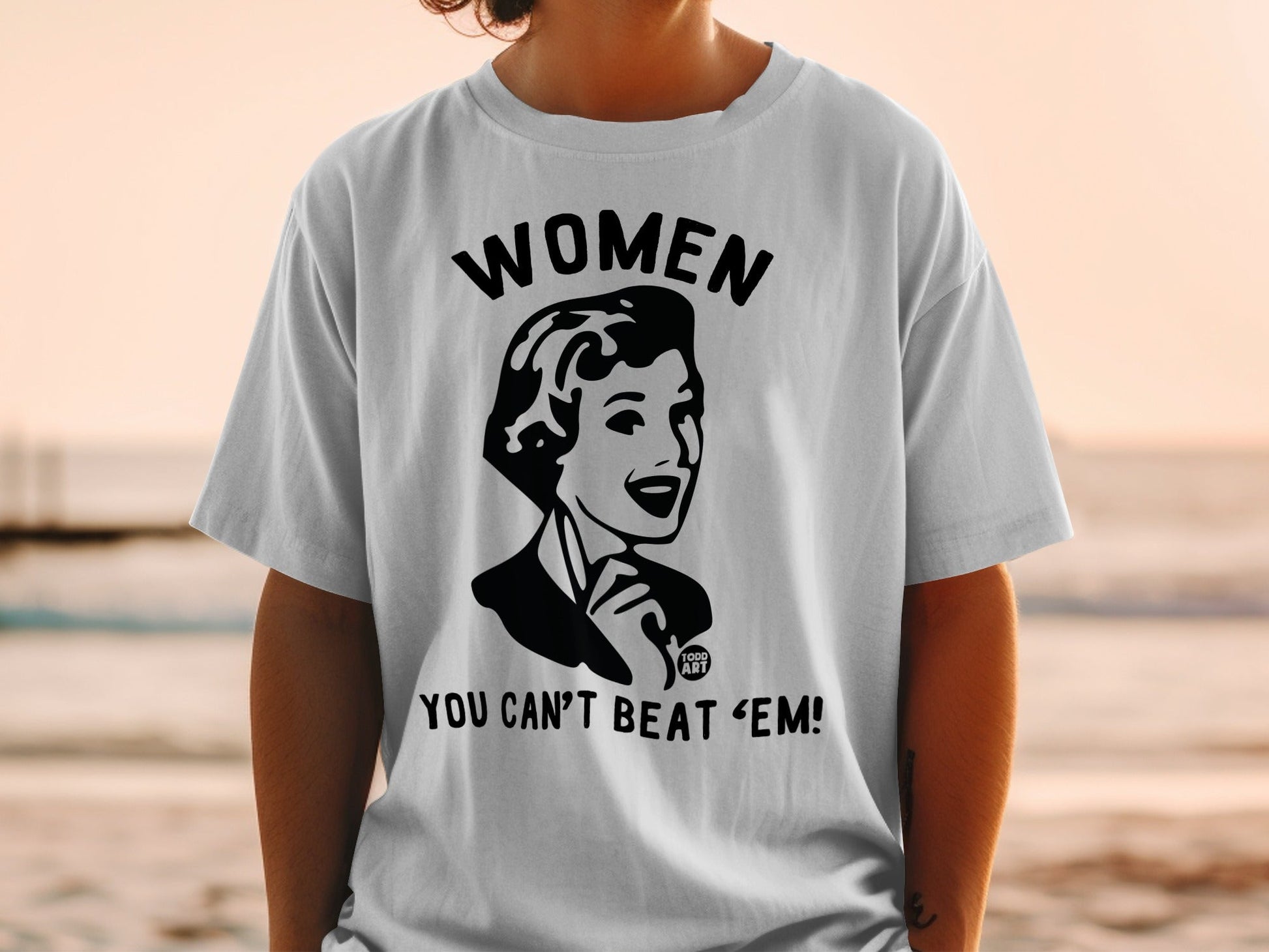 White t-shirt with black graphic of a woman and text "WOMEN YOU CAN'T BEAT 'EM!".