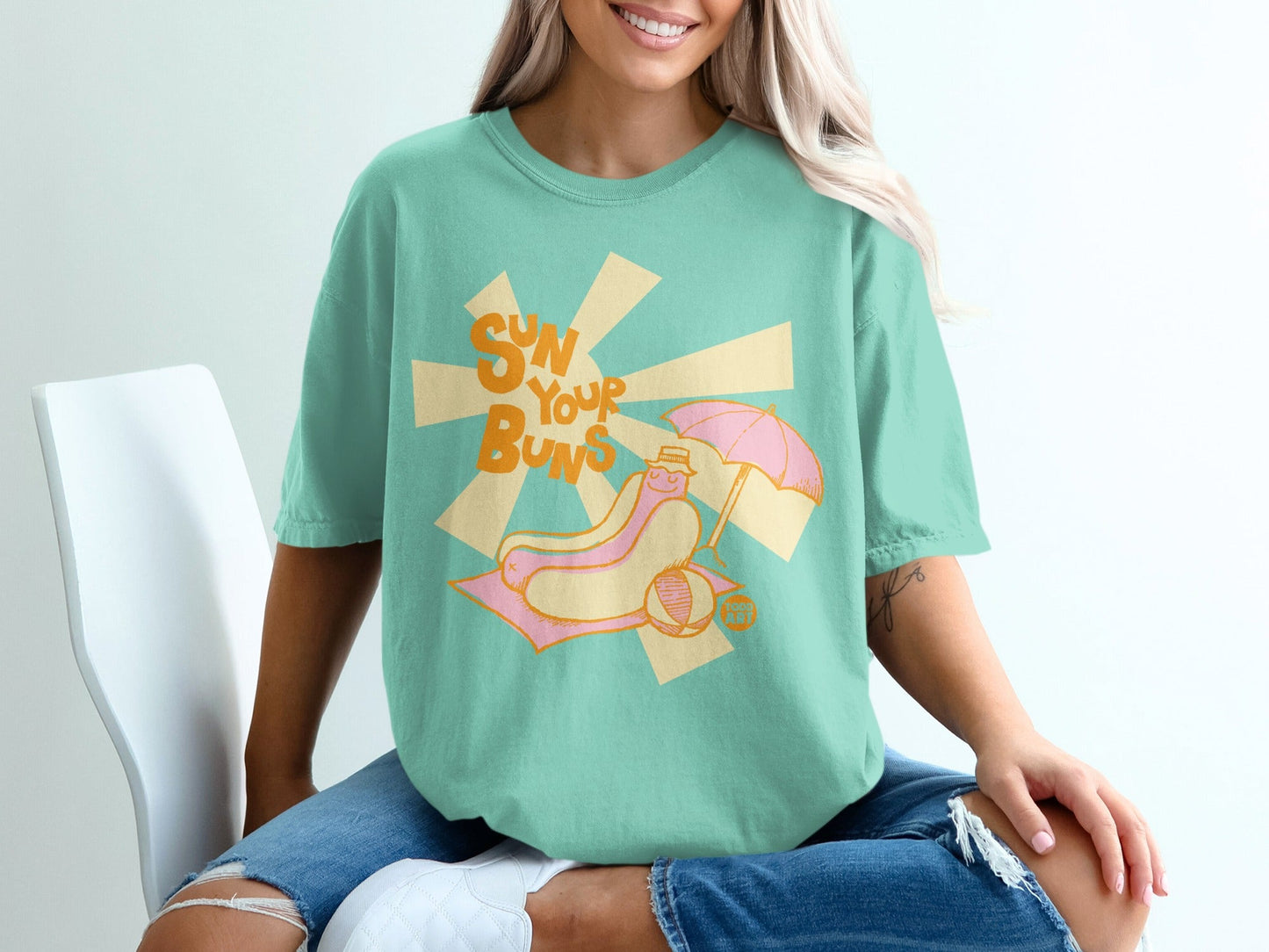 T-shirt with graphic of a hot dog on a beach towel under an umbrella.