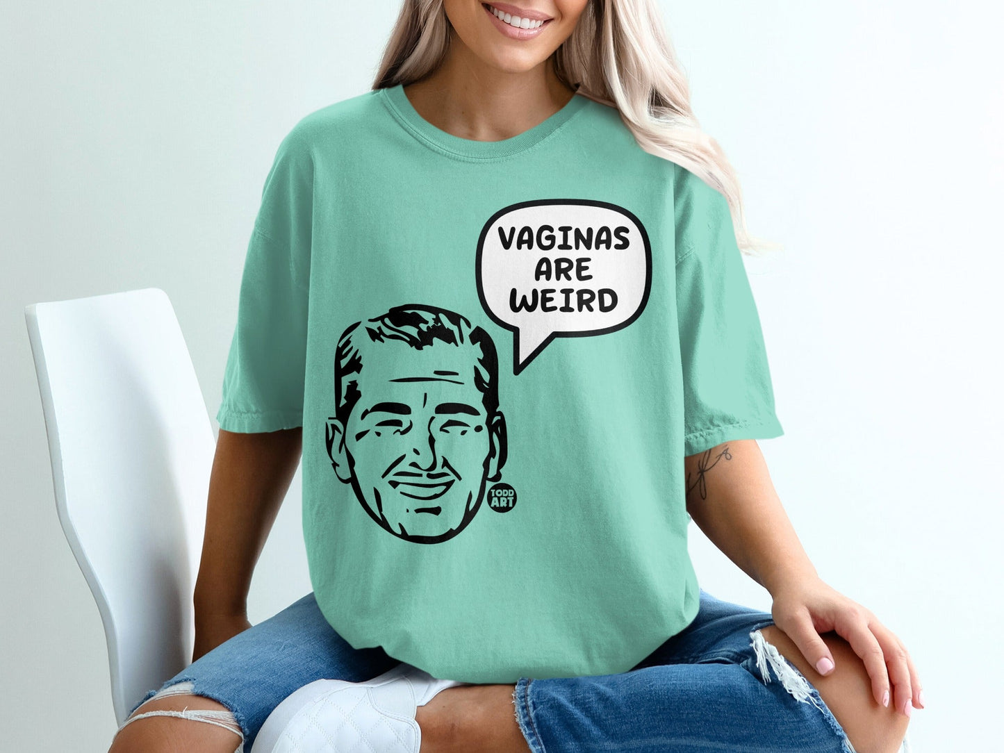 Mint green t-shirt with black line drawing of a man's head and "VAGINAS ARE WEIRD" in a speech bubble.