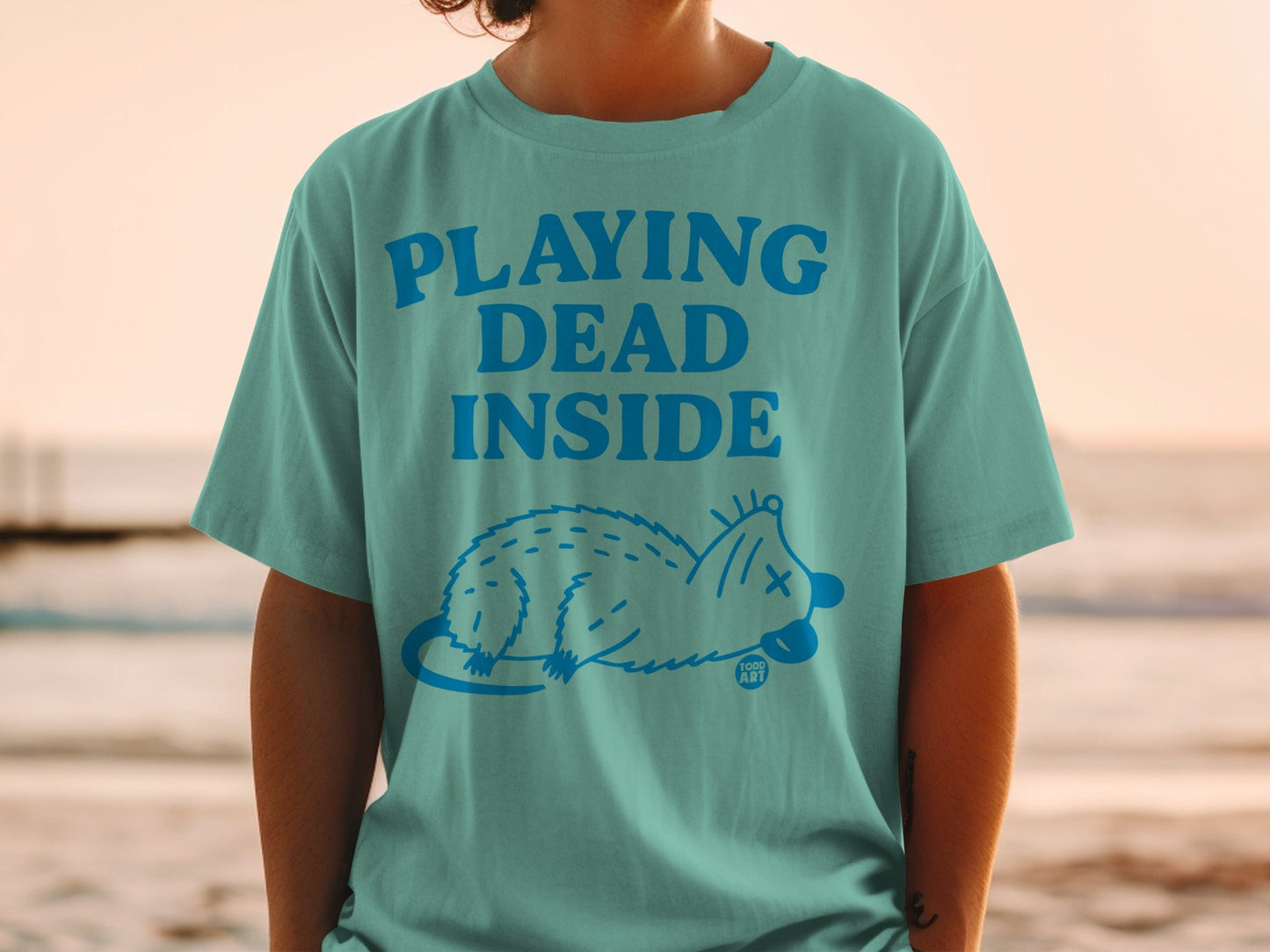 Teal t-shirt with "PLAYING DEAD INSIDE" text and opossum illustration.