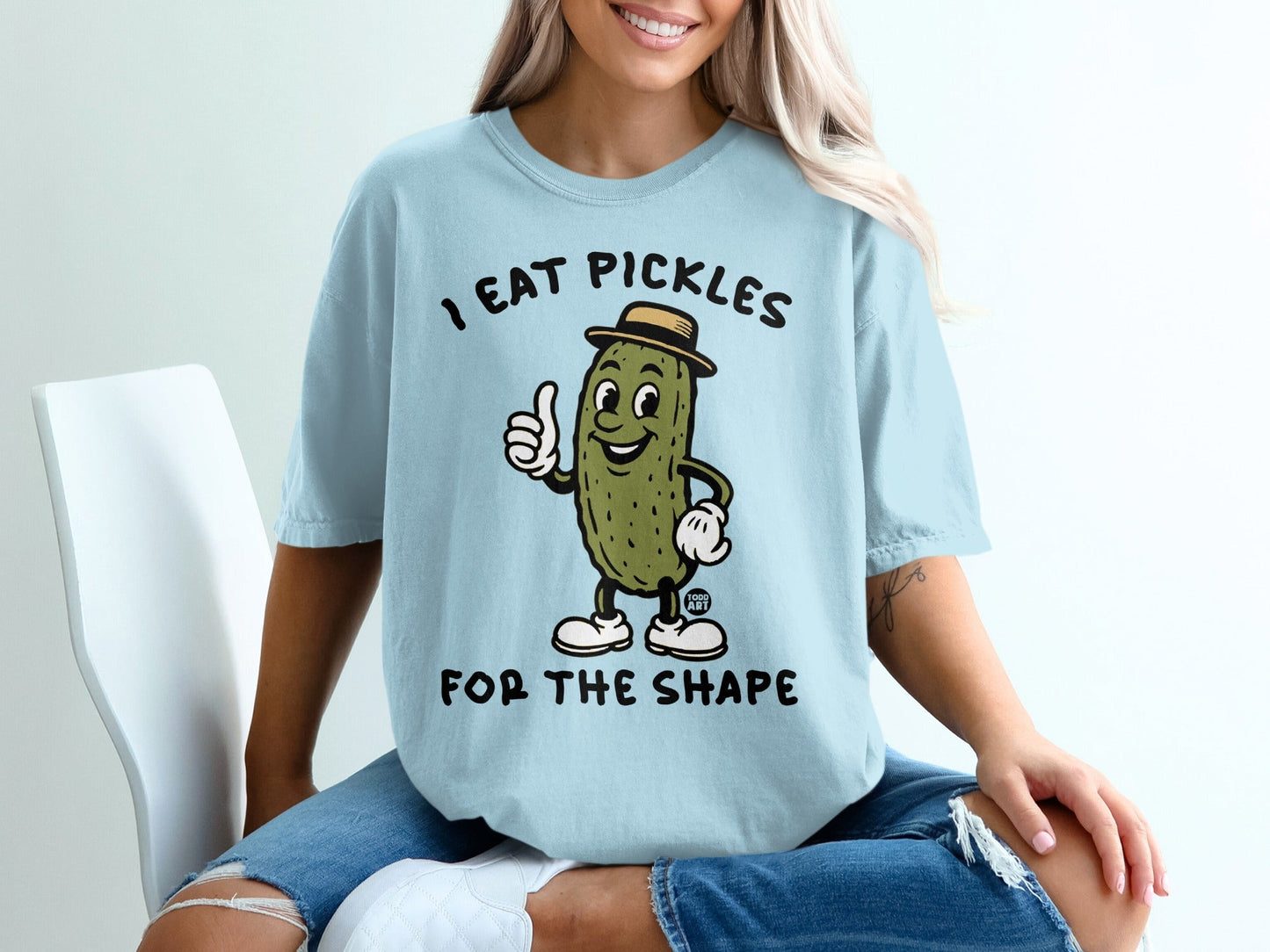 Light blue t-shirt with cartoon pickle giving a thumbs up and text "I EAT PICKLES FOR THE SHAPE".