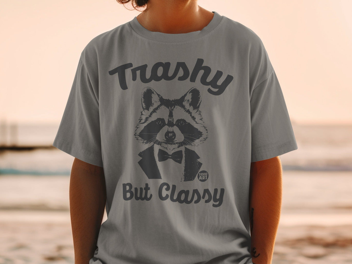 Grey t-shirt with a raccoon wearing a bowtie and text "Trashy But Classy".