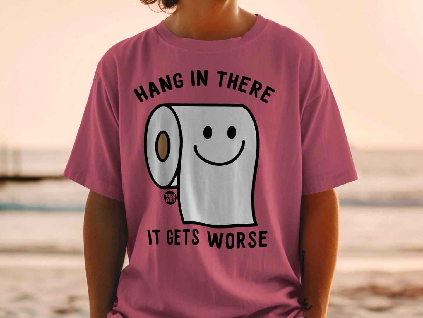 Pink t-shirt with a smiling toilet paper roll and text: "Hang in there, it gets worse."