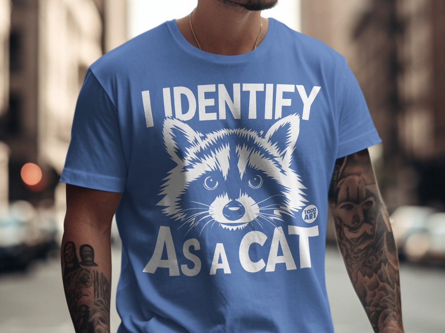 Blue t-shirt with white text "I IDENTIFY AS A CAT" and a raccoon face graphic.