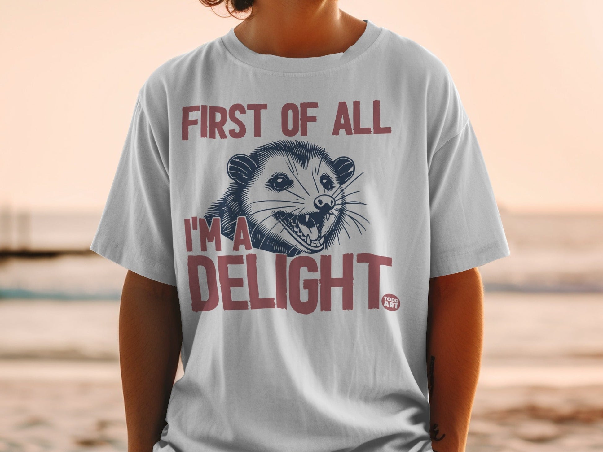 White t-shirt with possum graphic and text "First of all I'm a DELIGHT".