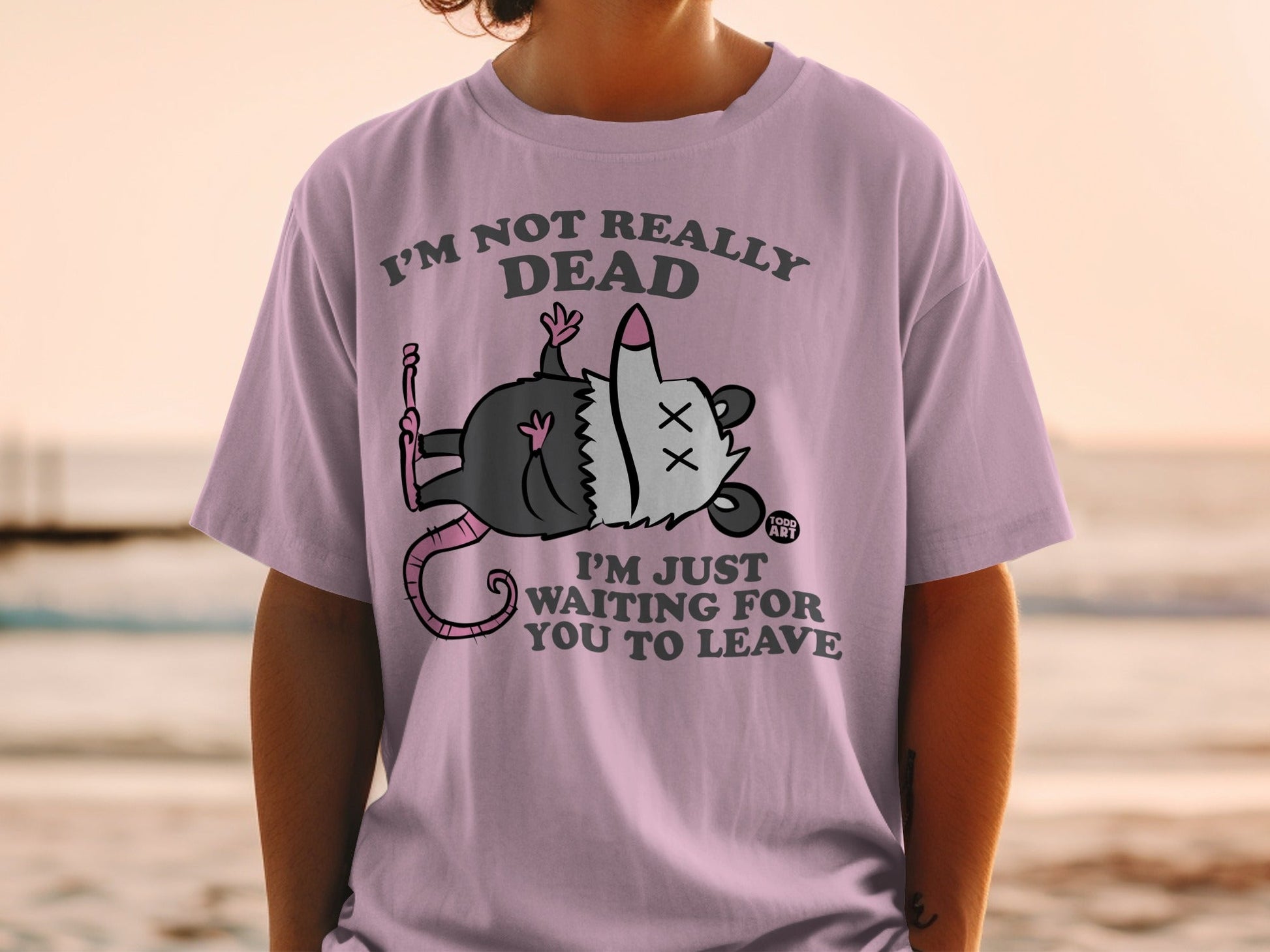 Pink t-shirt with opossum playing dead and text "I'm not really dead, I'm just waiting for you to leave."