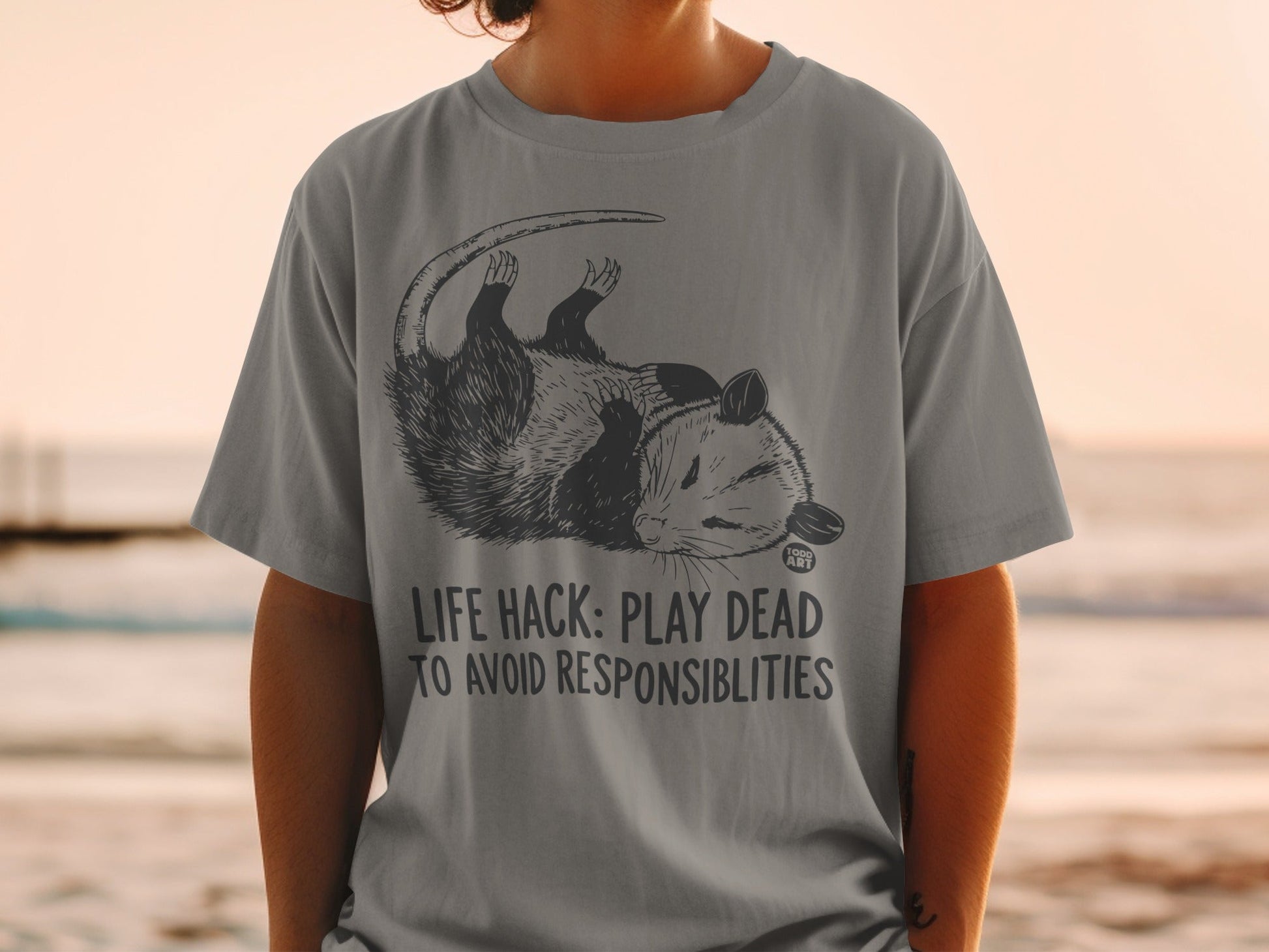 T-shirt with opossum illustration and text "LIFE HACK: PLAY DEAD TO AVOID RESPONSIBILITIES".