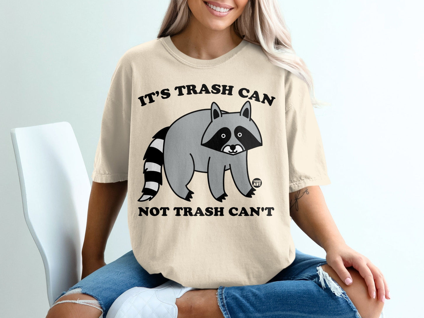 Cream t-shirt with raccoon graphic and text "IT'S TRASH CAN NOT TRASH CAN'T".