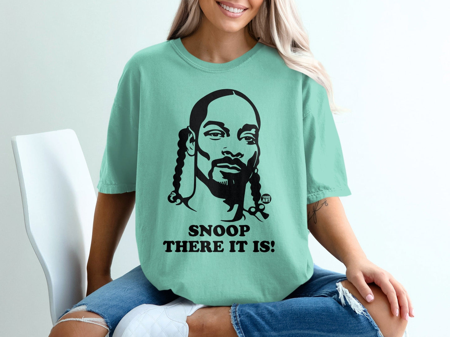 Teal t-shirt with black graphic of Snoop Dogg and text "SNOOP THERE IT IS!".
