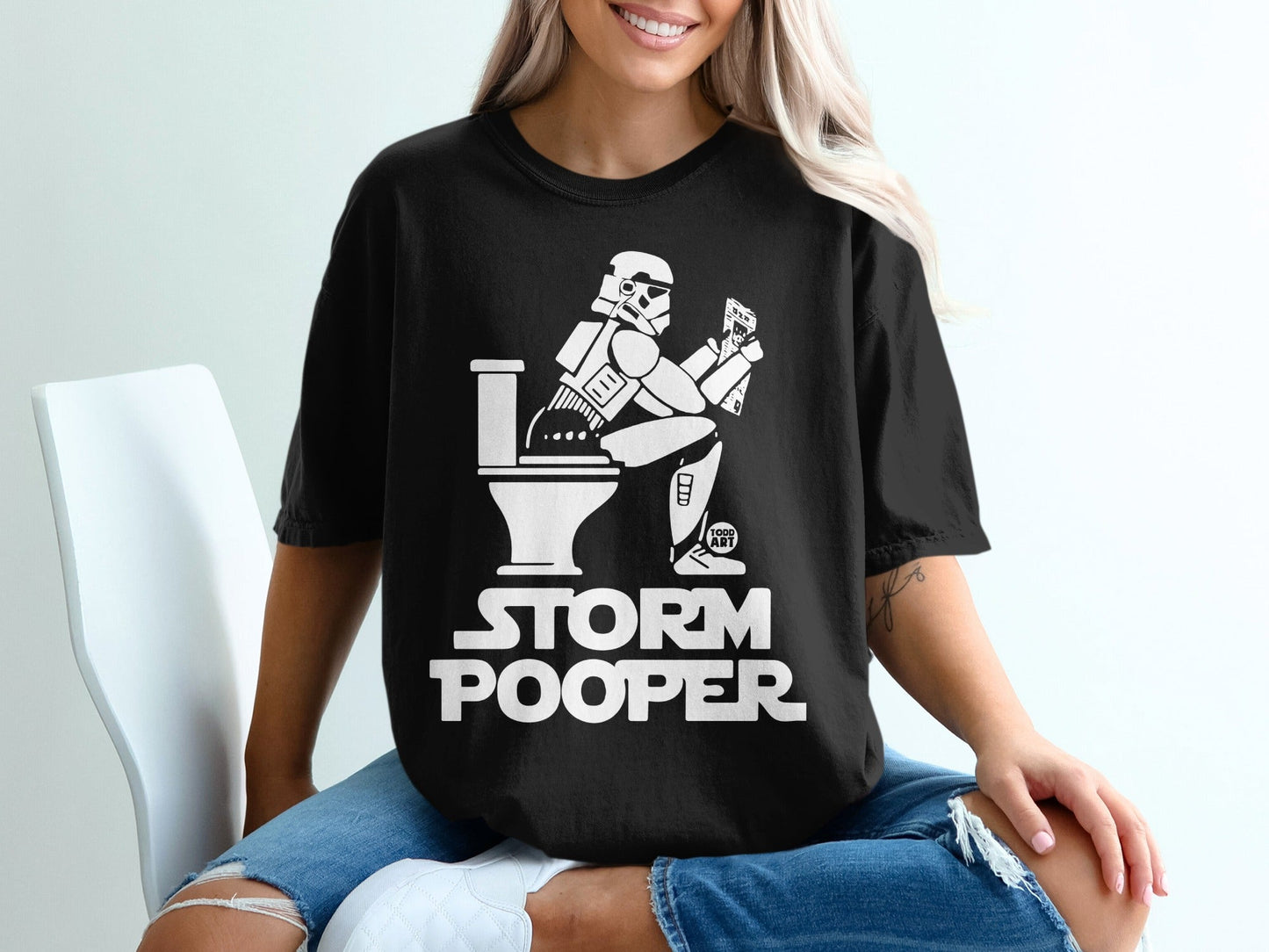 Stormtrooper sitting on toilet, text "STORM POOPER" on black t-shirt.