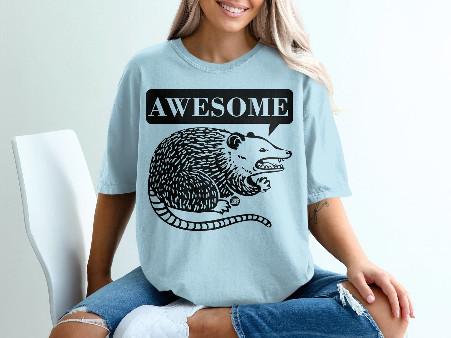Light blue t-shirt with a black opossum graphic and "AWESOME" speech bubble.