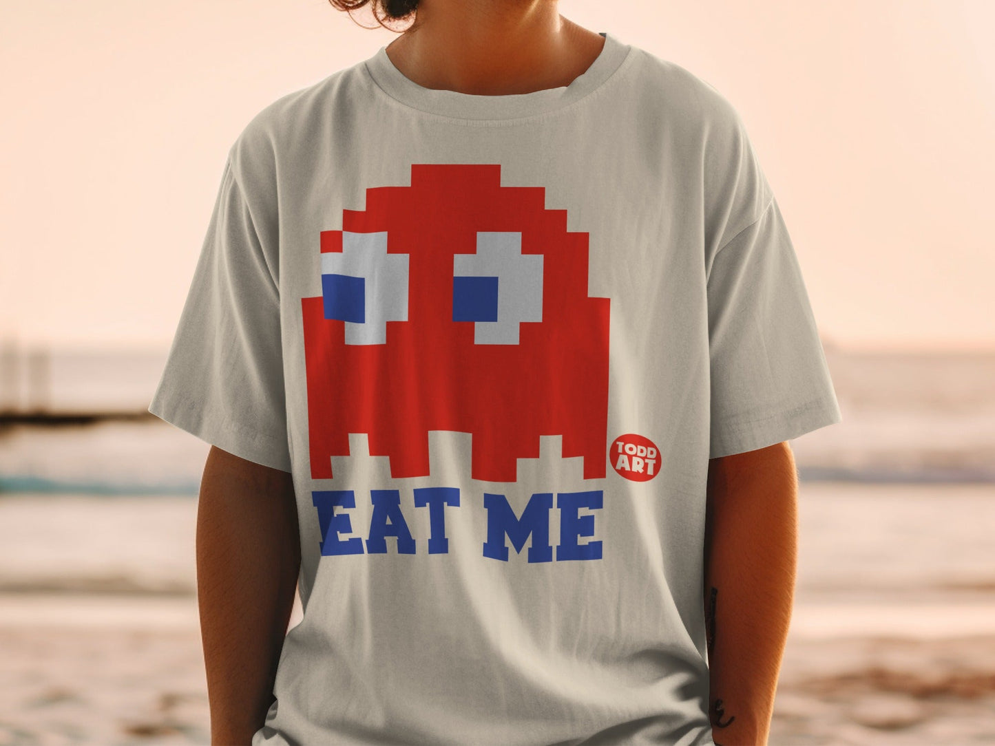 Red Pac-Man ghost character with "EAT ME" text on a t-shirt.