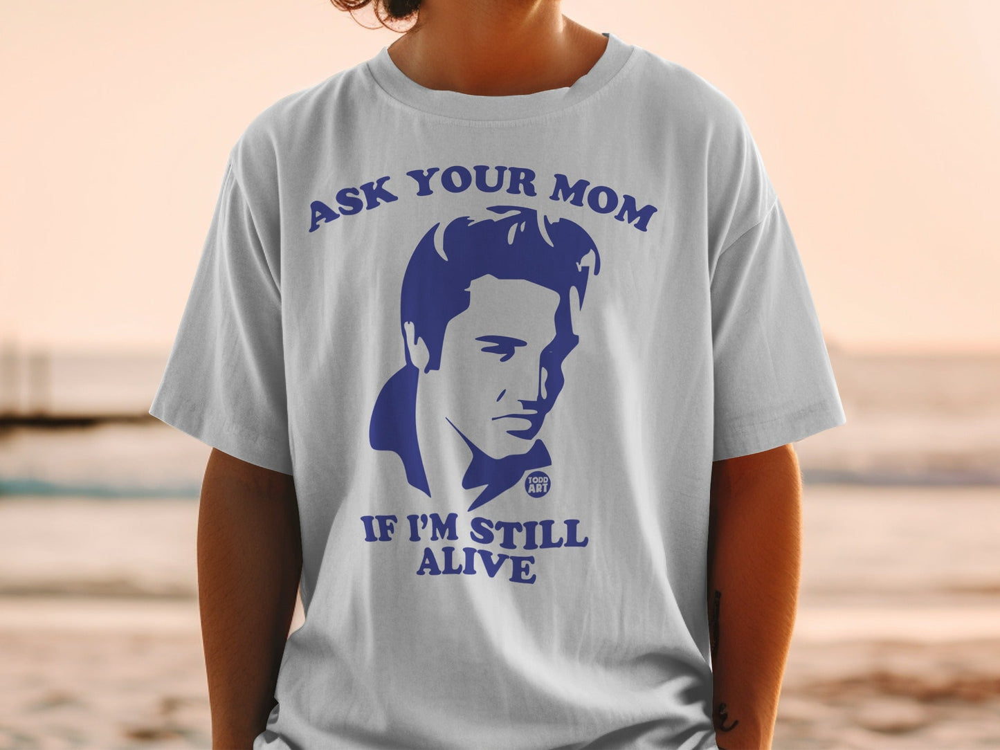 White t-shirt with blue graphic of Elvis Presley and text "ASK YOUR MOM IF I'M STILL ALIVE"